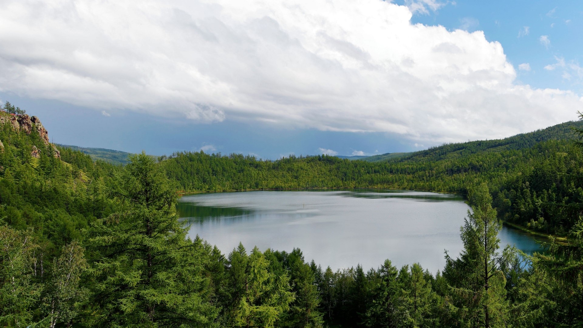 Lake surrounded by green forest and mountains under cloudy sky HD Wallpaper