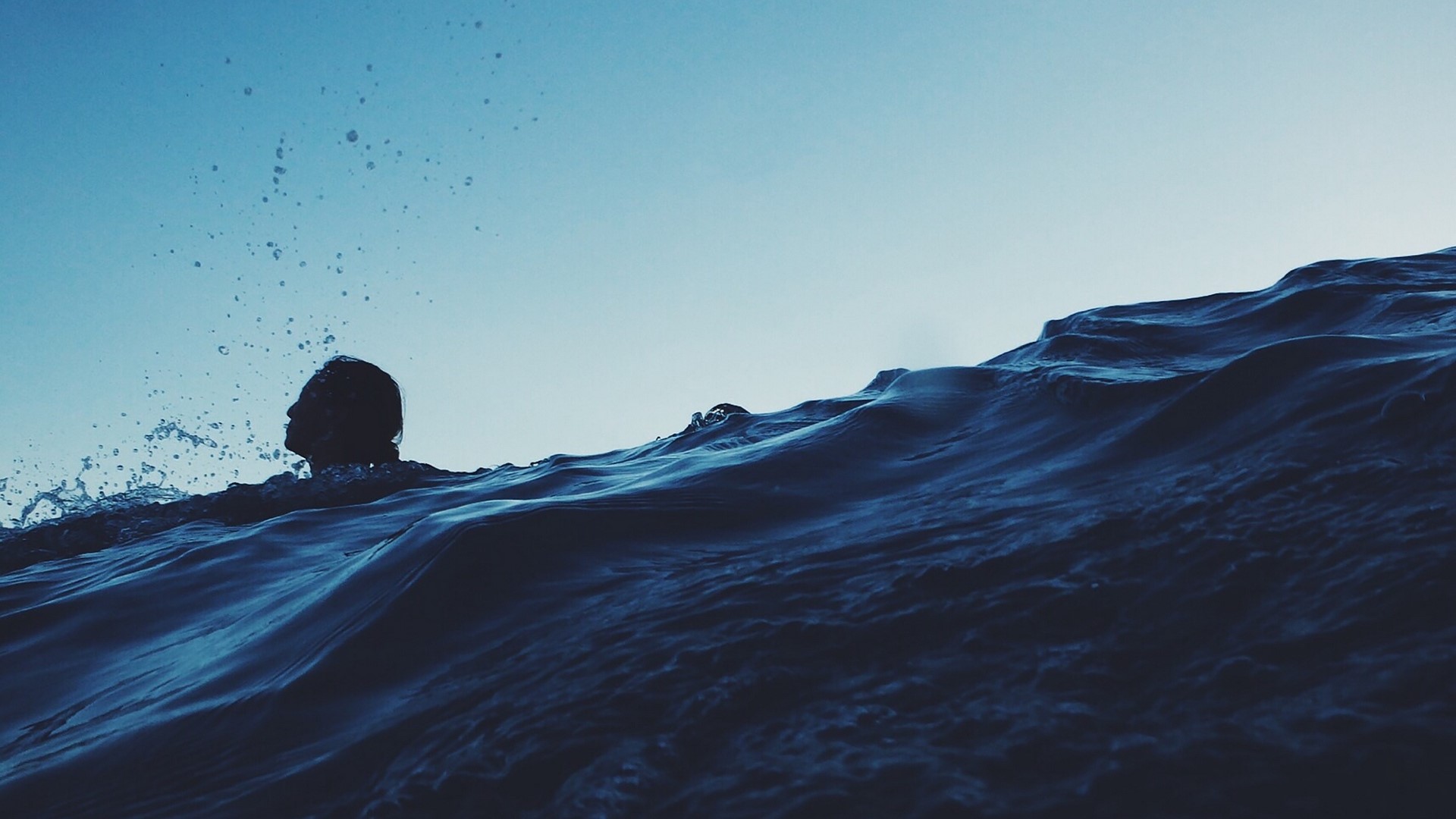 Silhouette of a person swimming in dark ocean waves HD Wallpaper