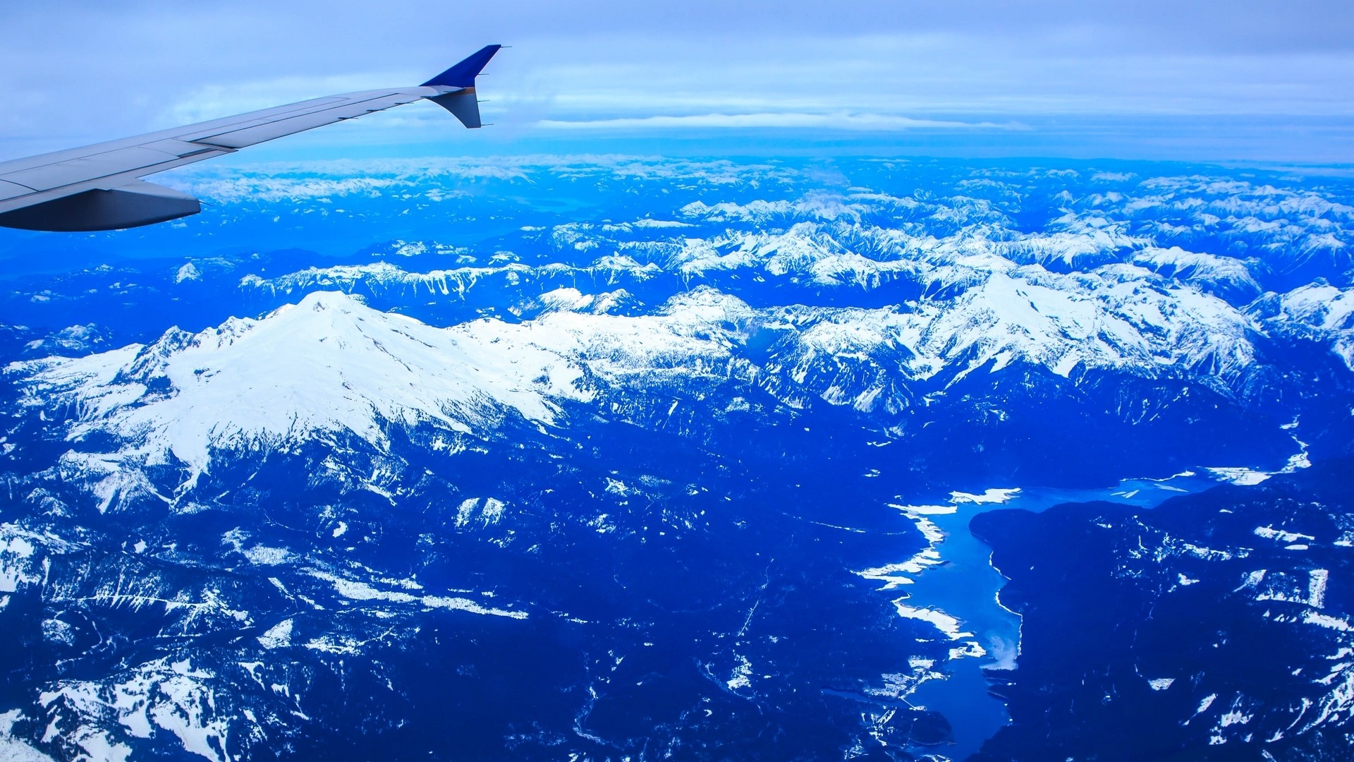 Airplane wing over snow-capped mountains and lake HD Wallpaper