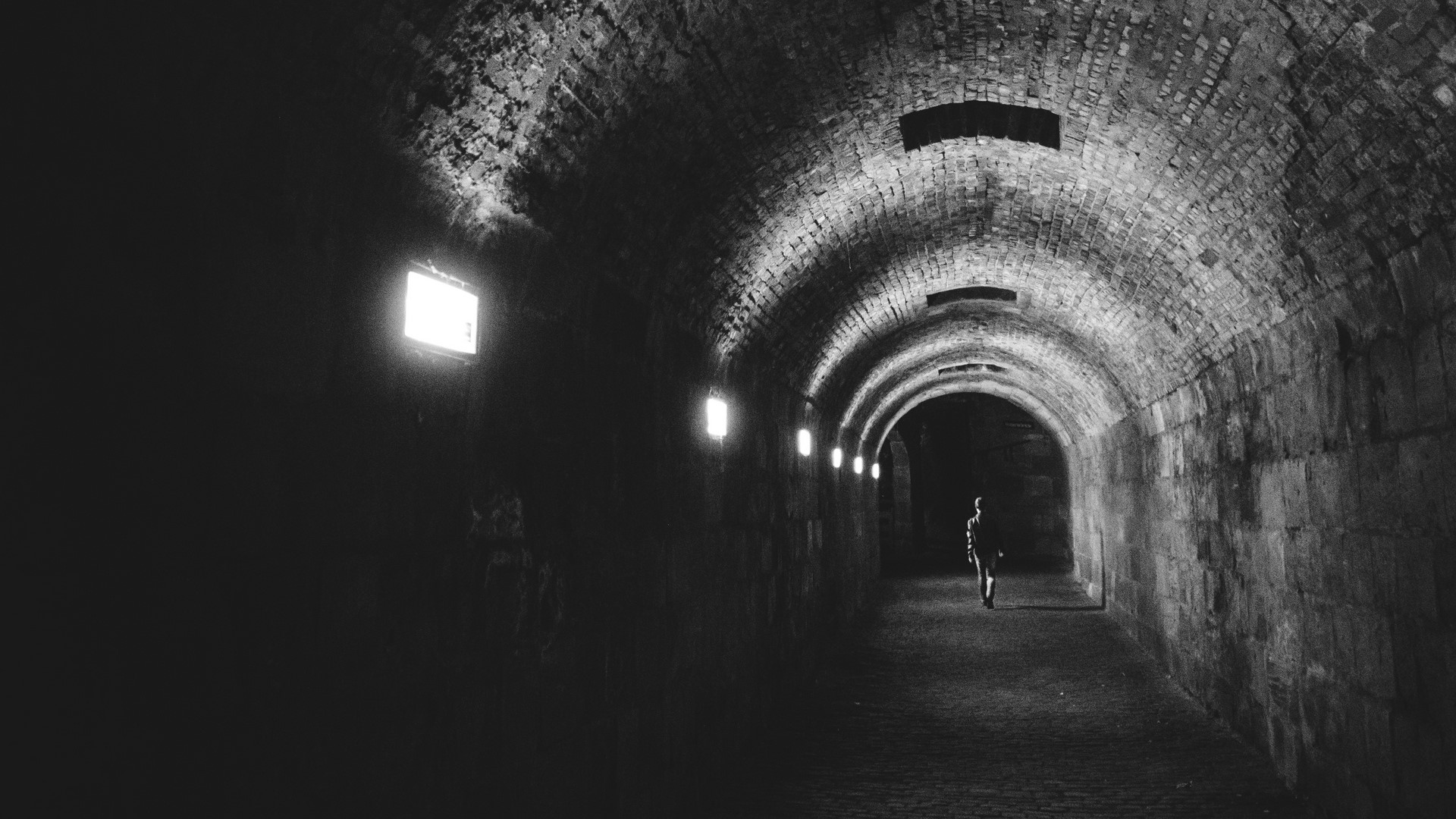 Man walking in a dark brick tunnel HD Wallpaper