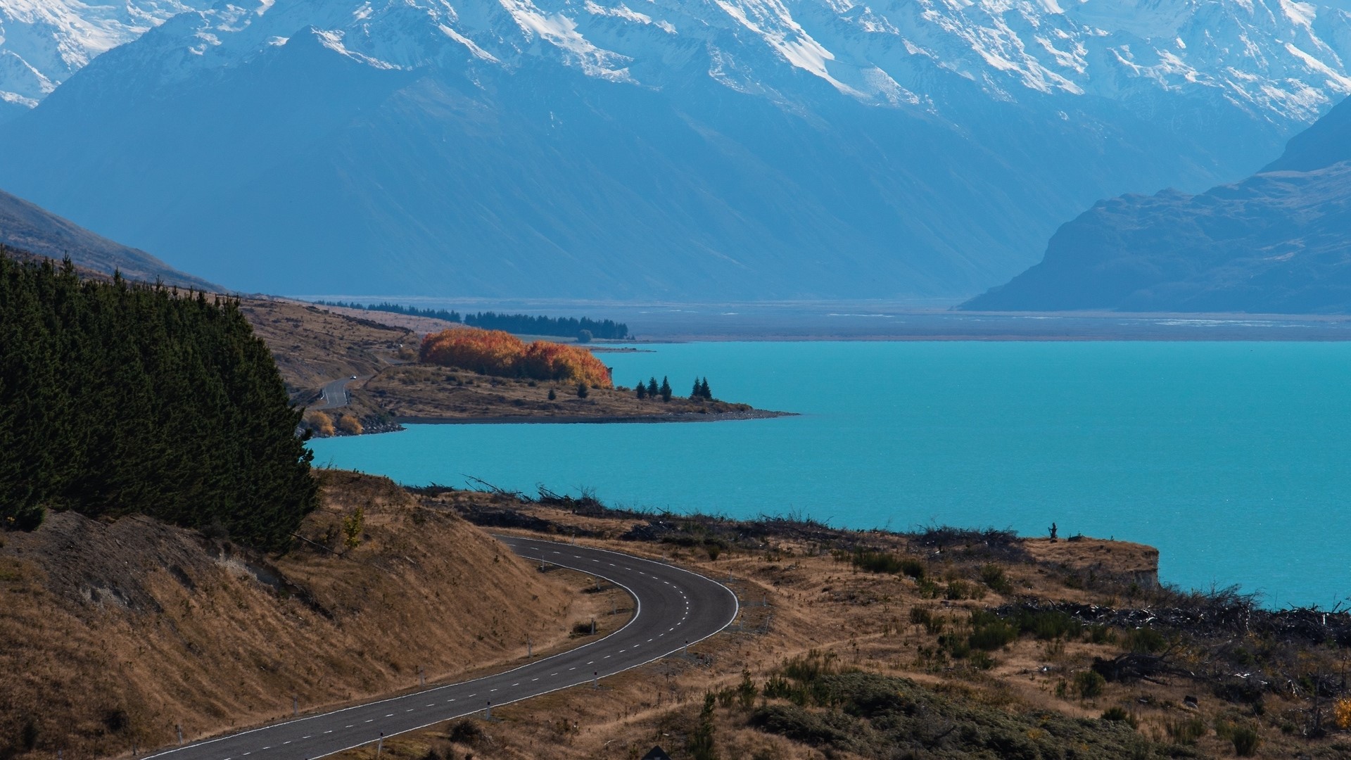 Road curving towards turquoise lake with snow-capped mountains in New Zealand HD Wallpaper