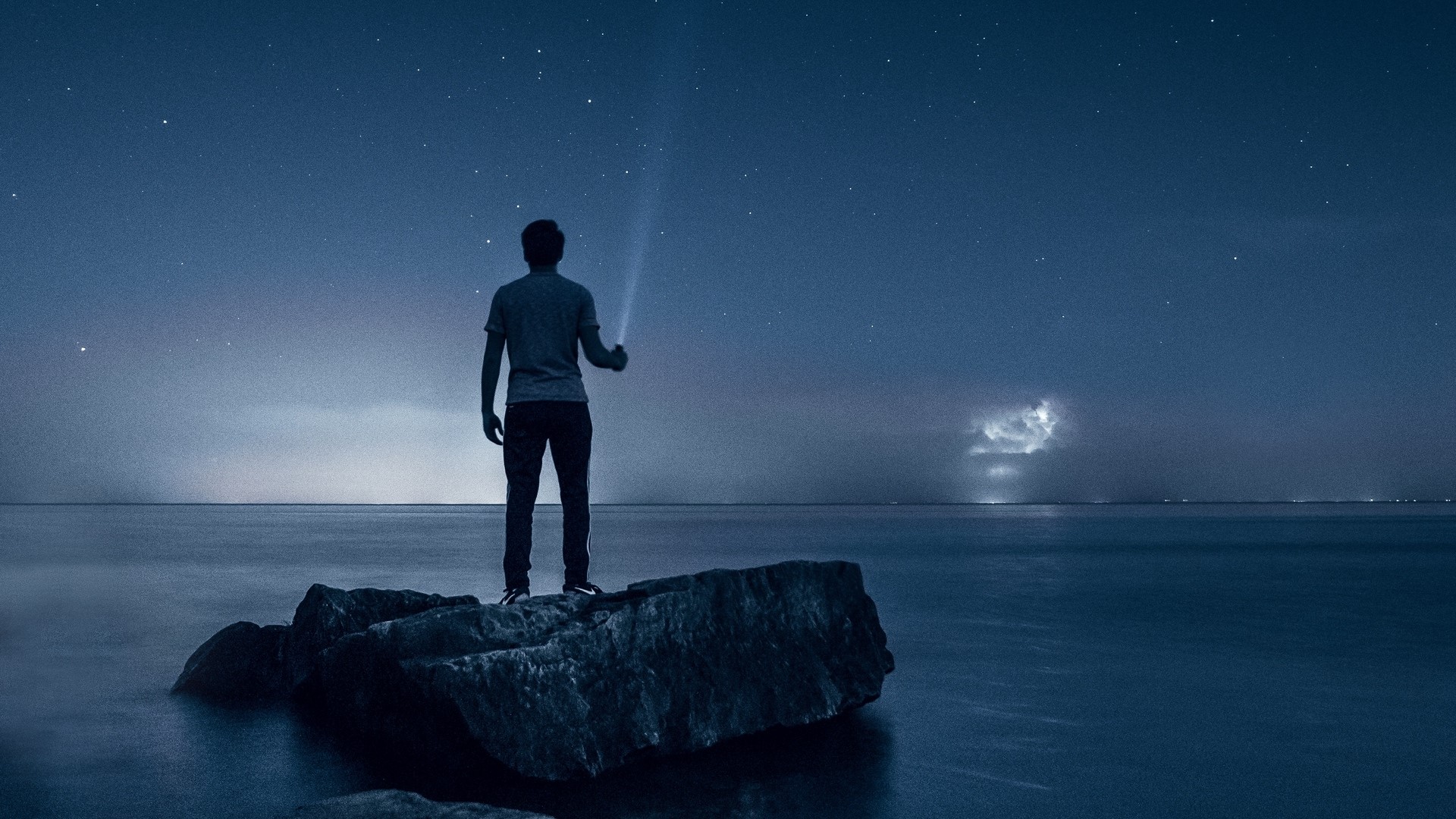 Man with flashlight on rocks at night HD Wallpaper