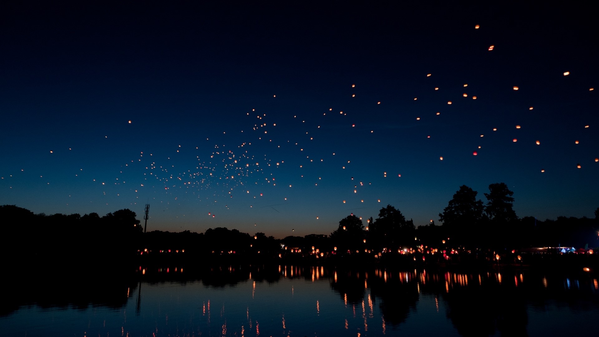 Chinese lanterns floating in the night sky over a lake HD Wallpaper