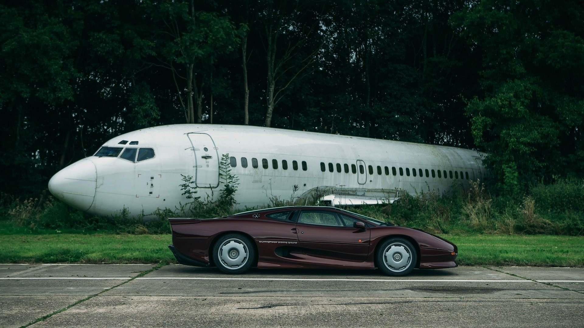 Jaguar XJ220 parked next to a derelict airplane HD Wallpaper