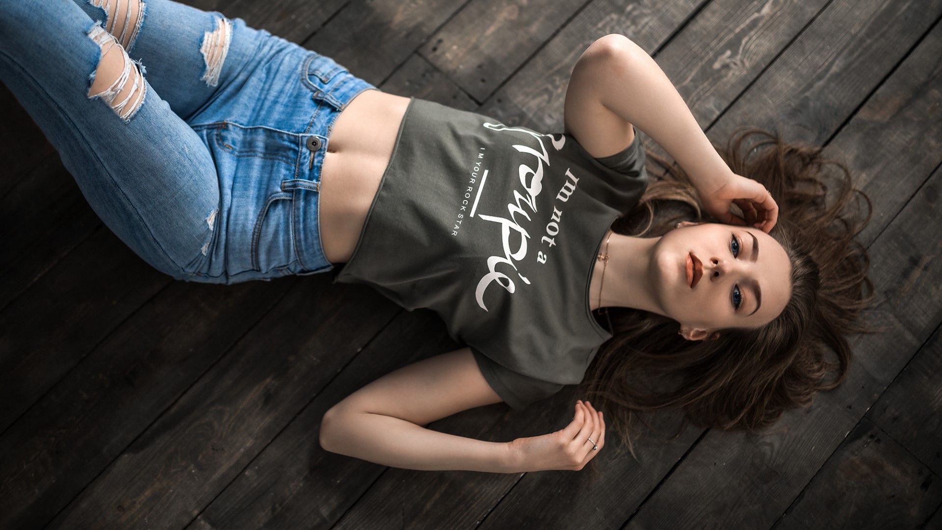Girl in ripped jeans and crop top lying on wooden floor HD Wallpaper