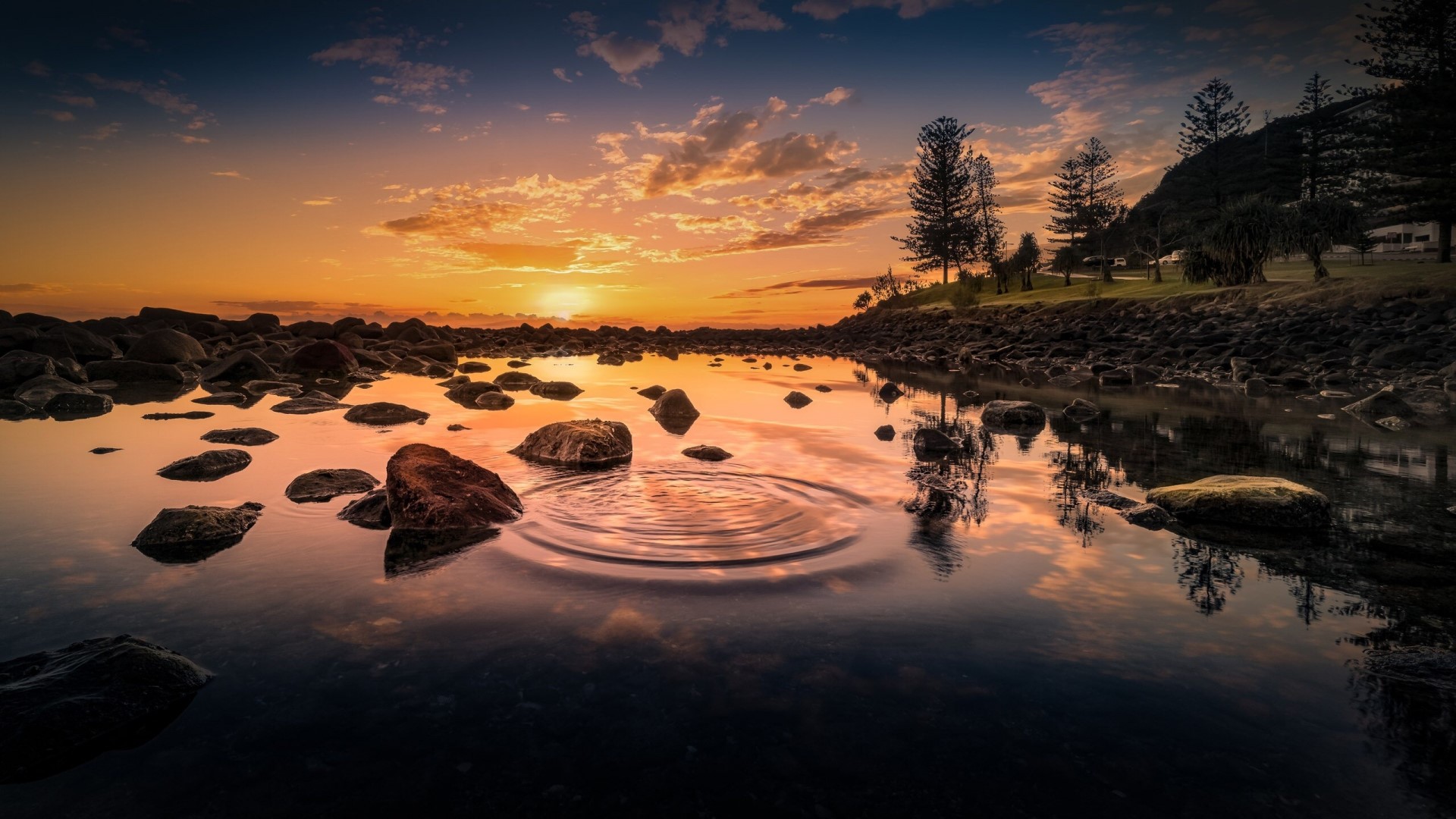 Sunset over rocky shore with water ripples HD Wallpaper