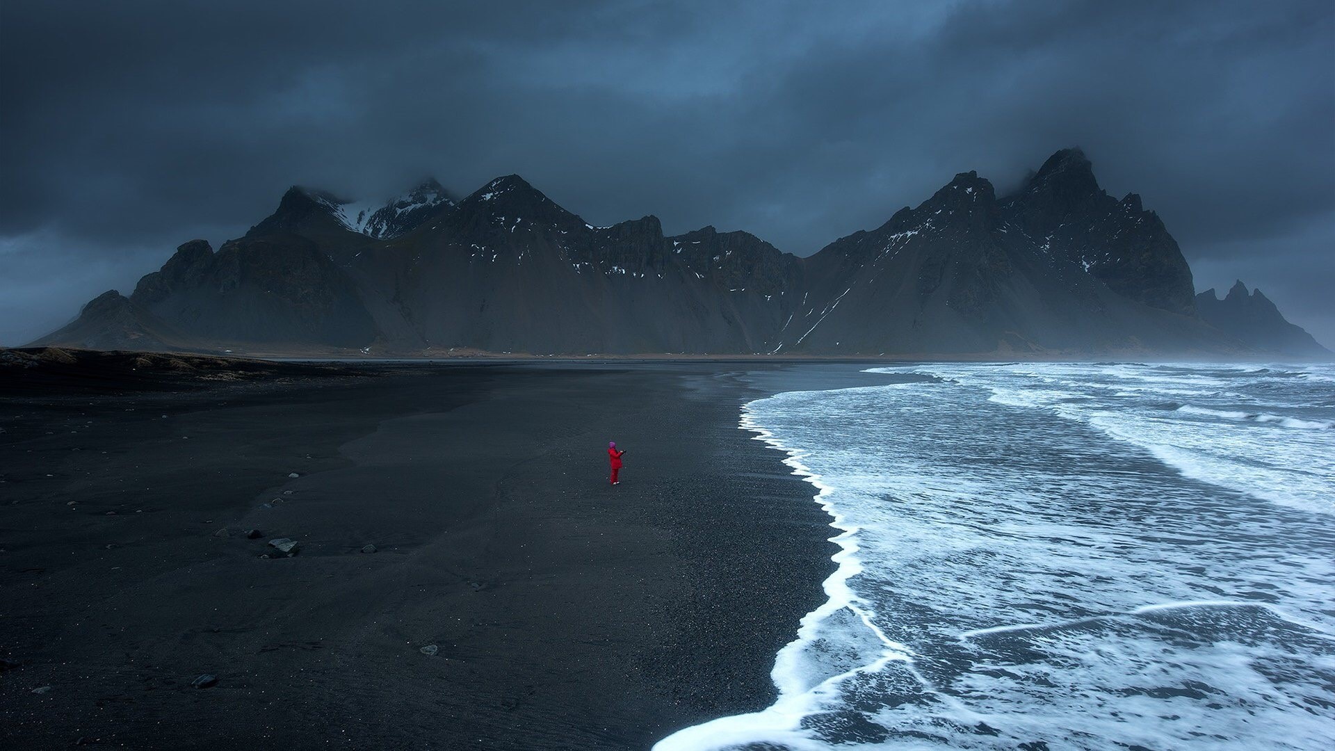 Person in red on black sand beach with Vestrahorn mountains, Iceland HD Wallpaper