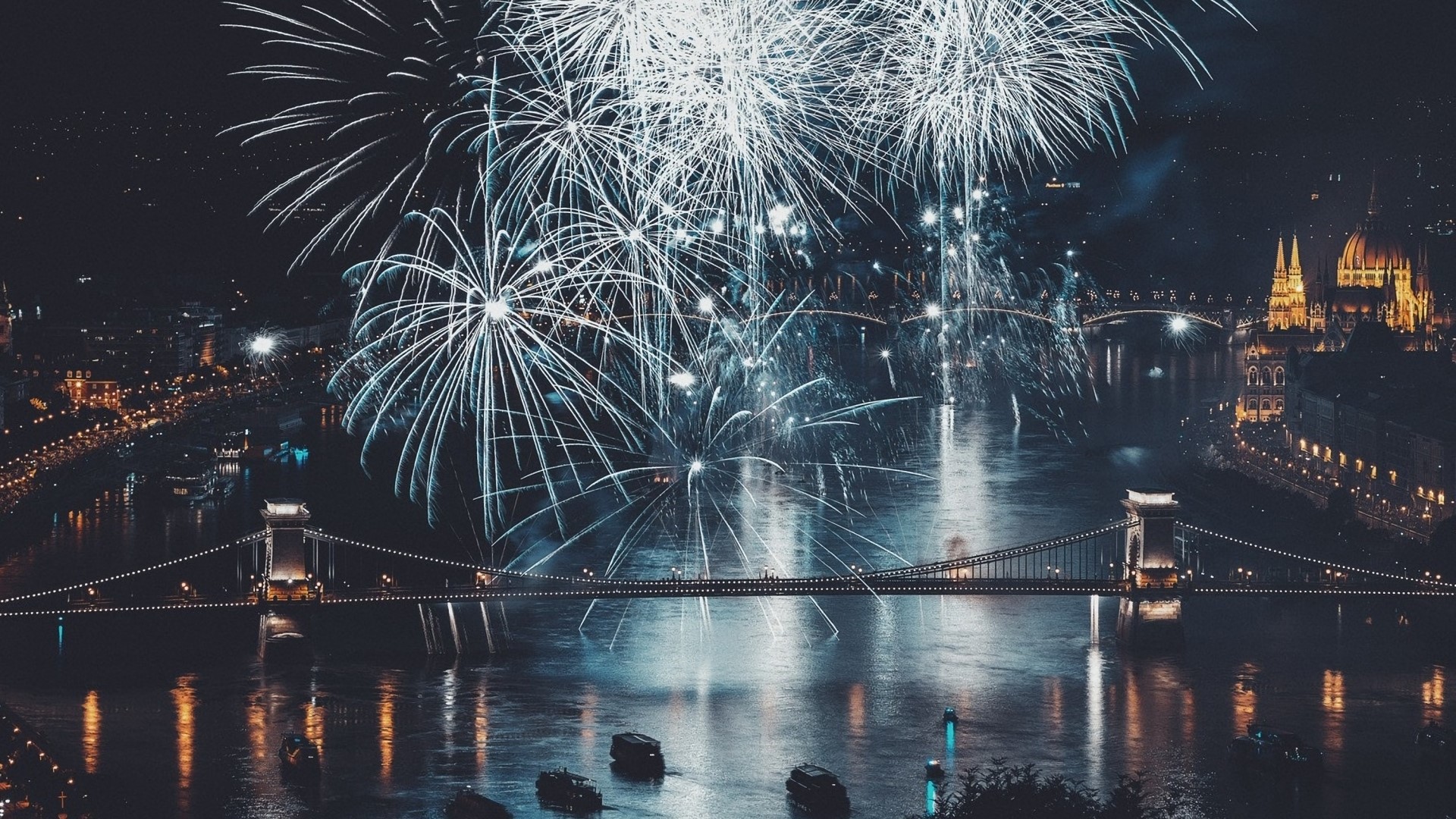 Fireworks over a city and river at night HD Wallpaper