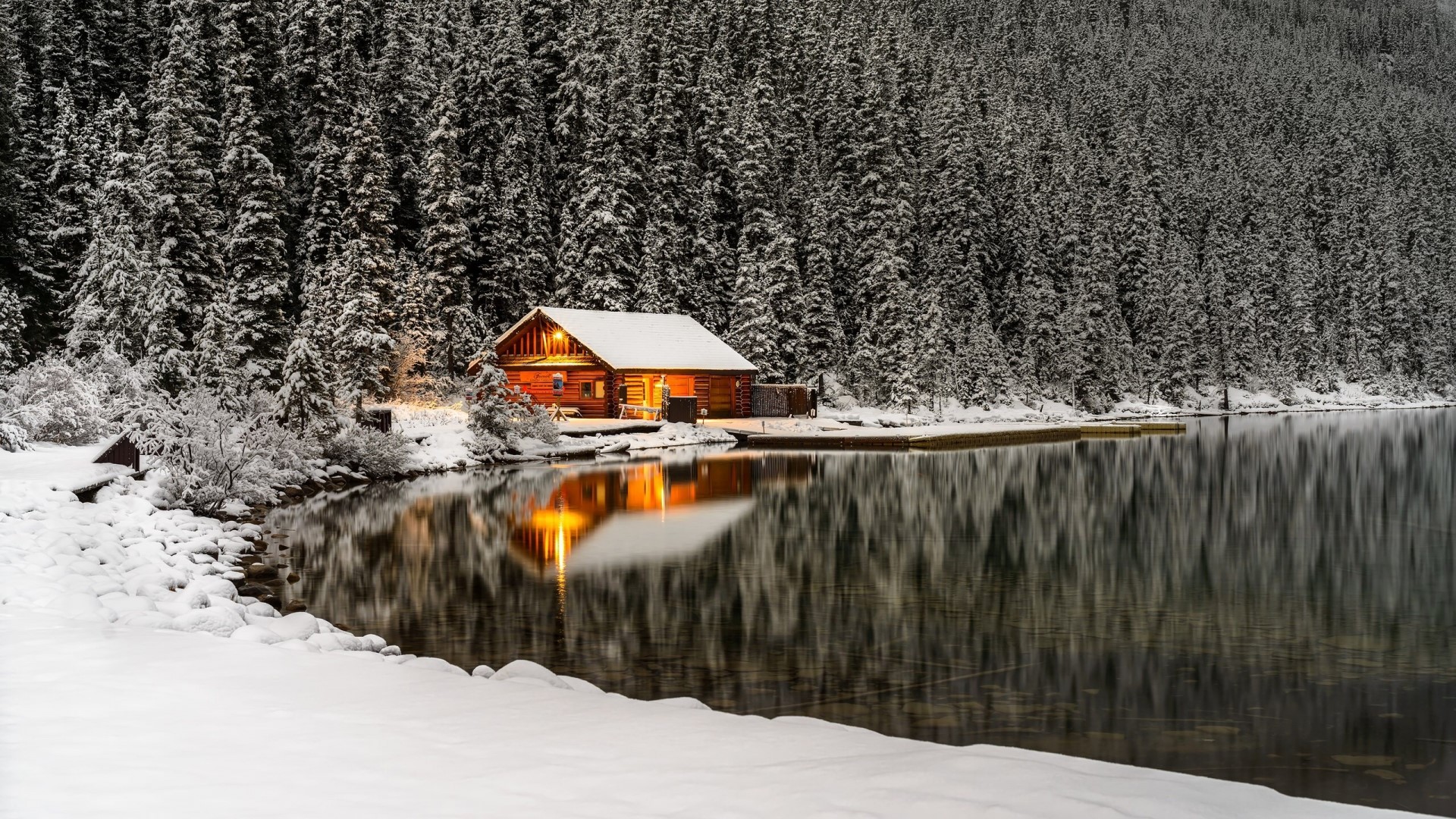 Log cabin by a snowy lake with pine forest reflection HD Wallpaper