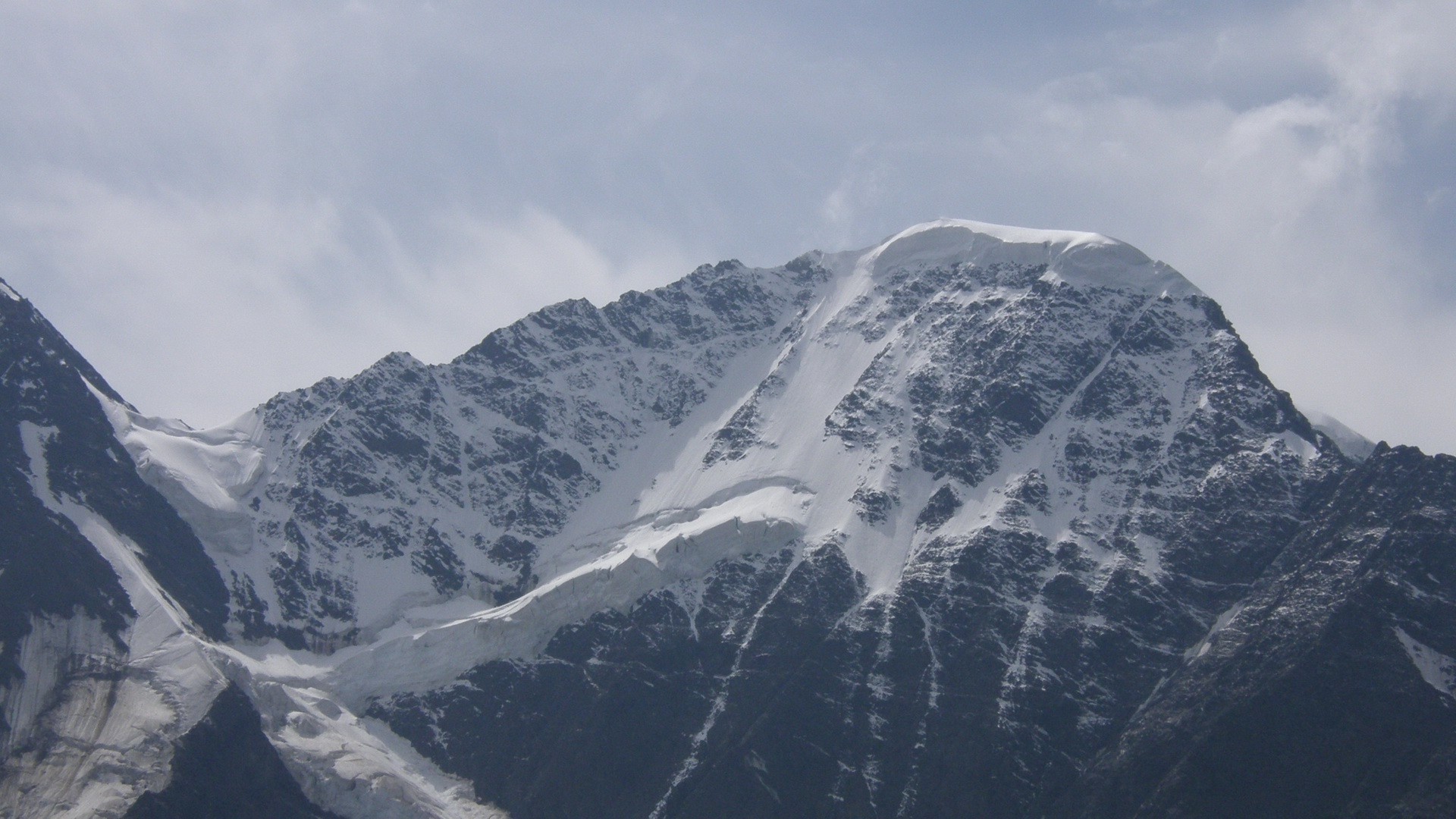 Snow-covered mountain range under a cloudy sky HD Wallpaper