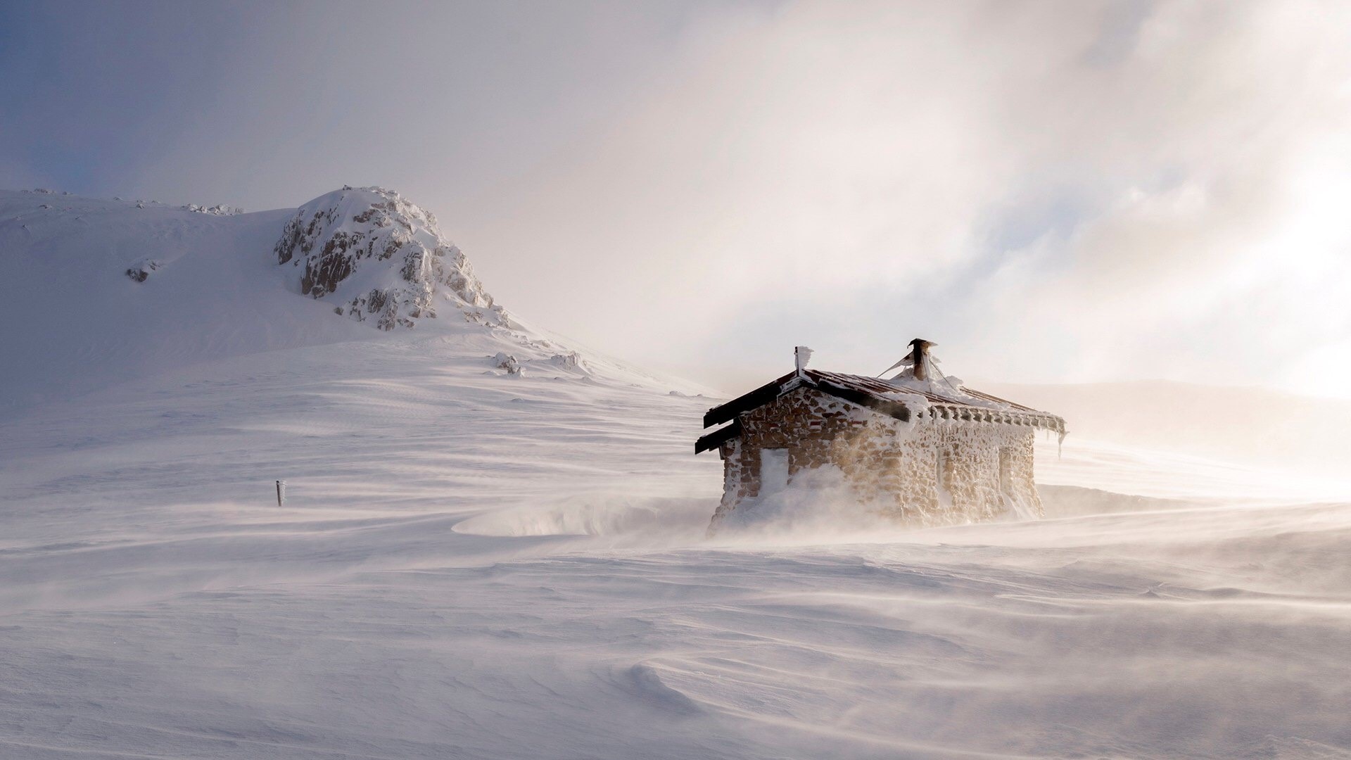 Stone cabin in a blizzard on a snowy mountain HD Wallpaper