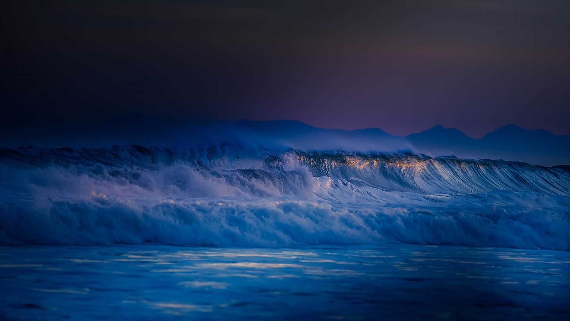 Crashing ocean waves at dusk with mountains in the background HD Wallpaper
