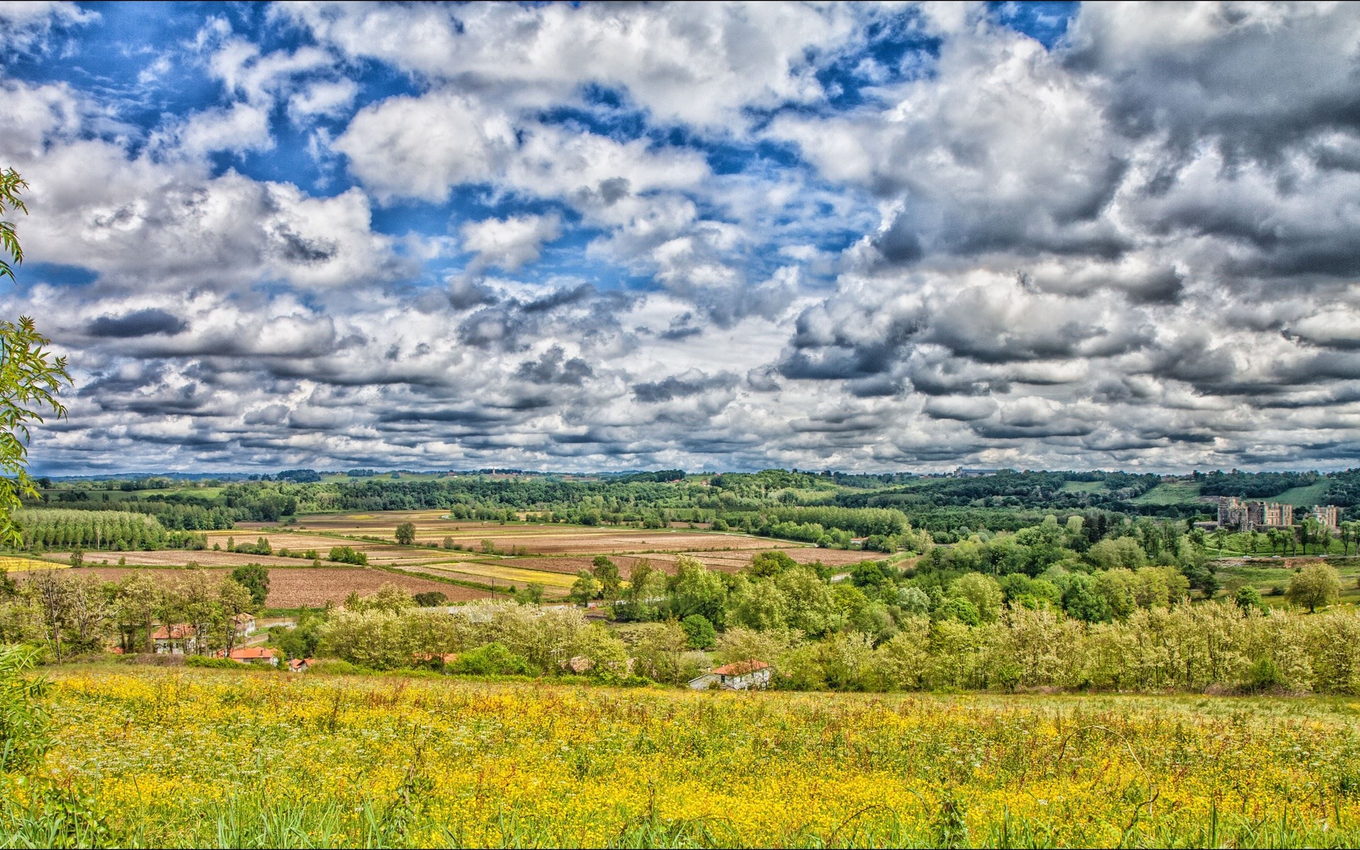 Rolling hills with fields and a castle under a cloudy sky HD Wallpaper