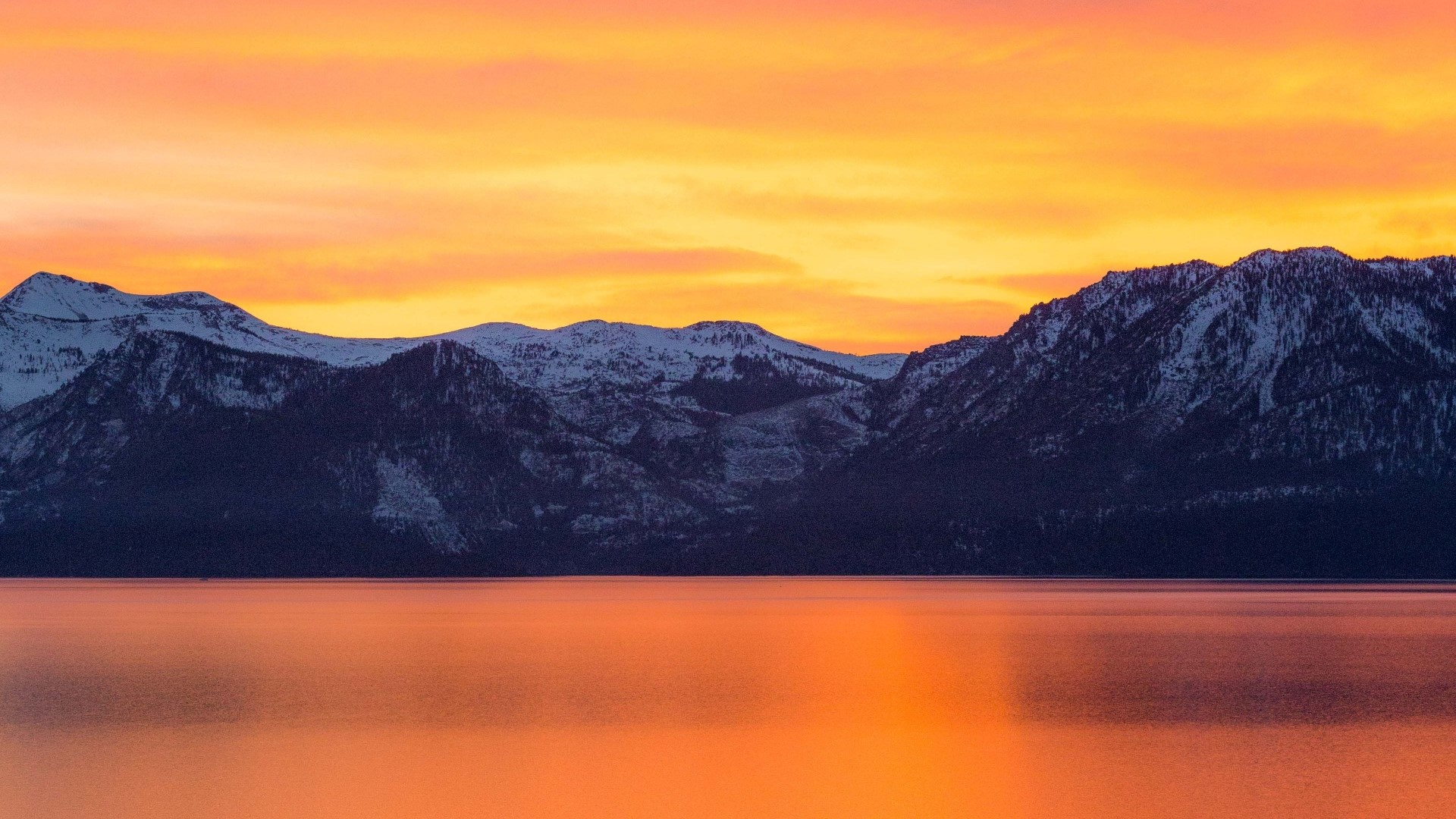 Snow-capped mountains reflected in a golden lake at sunset HD Wallpaper