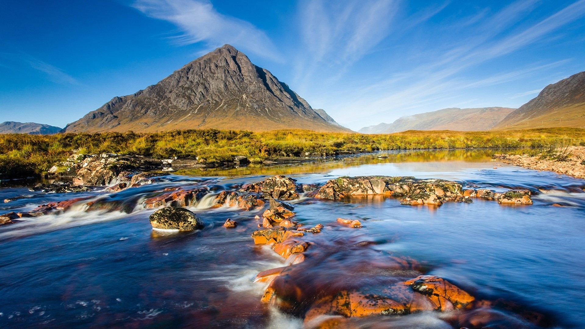 Mountain river with rocky foreground and golden hills HD Wallpaper