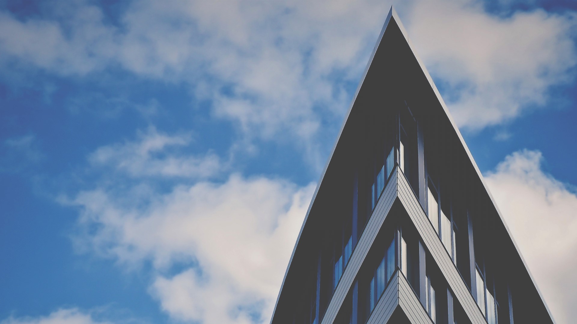 Modern building with sharp angles against a cloudy sky HD Wallpaper