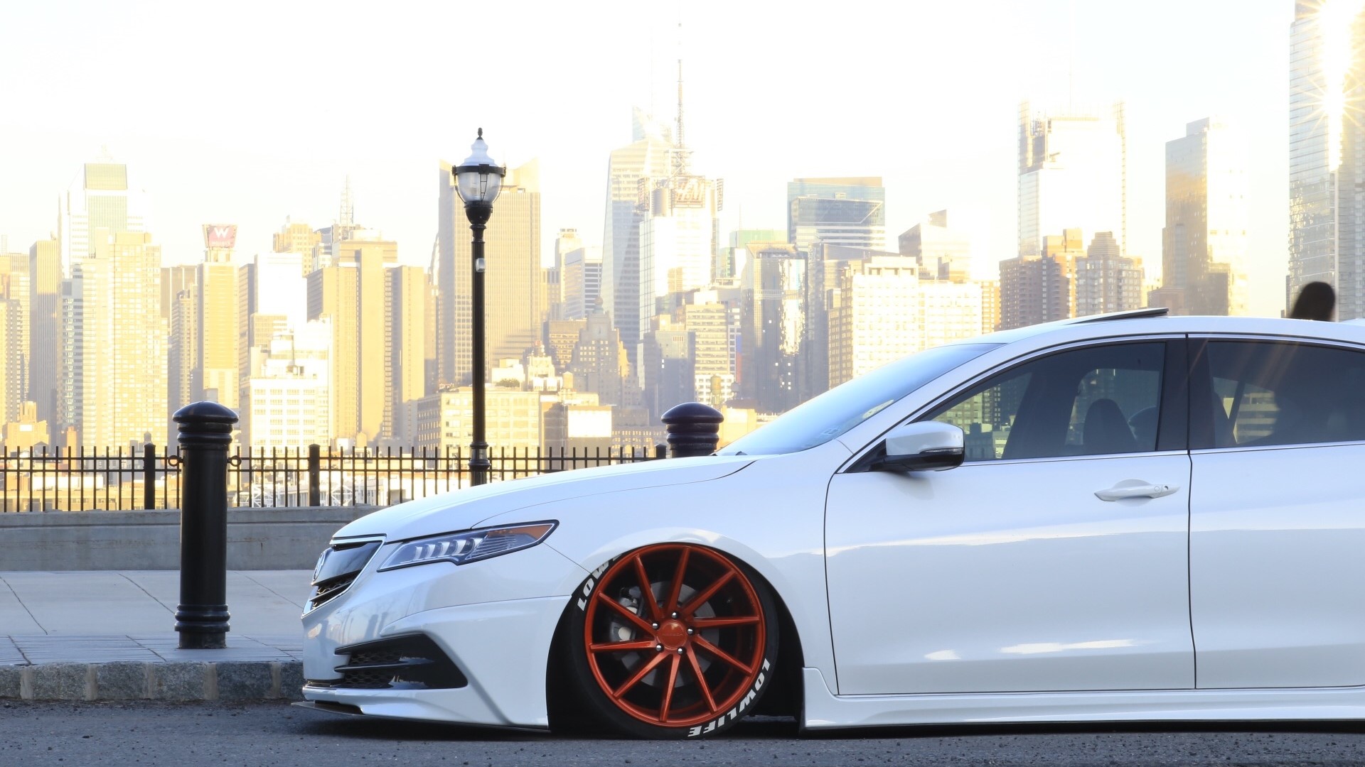 White Acura TLX with custom orange wheels in front of city skyline HD Wallpaper