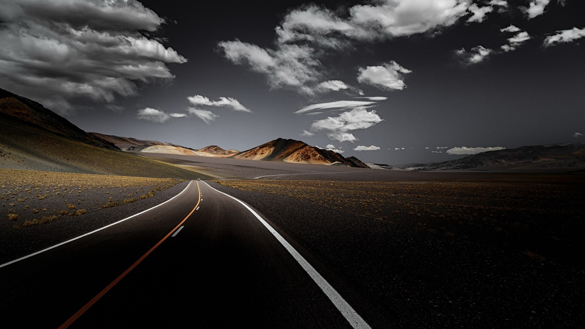 Road through a desolate landscape with mountains and clouds HD Wallpaper
