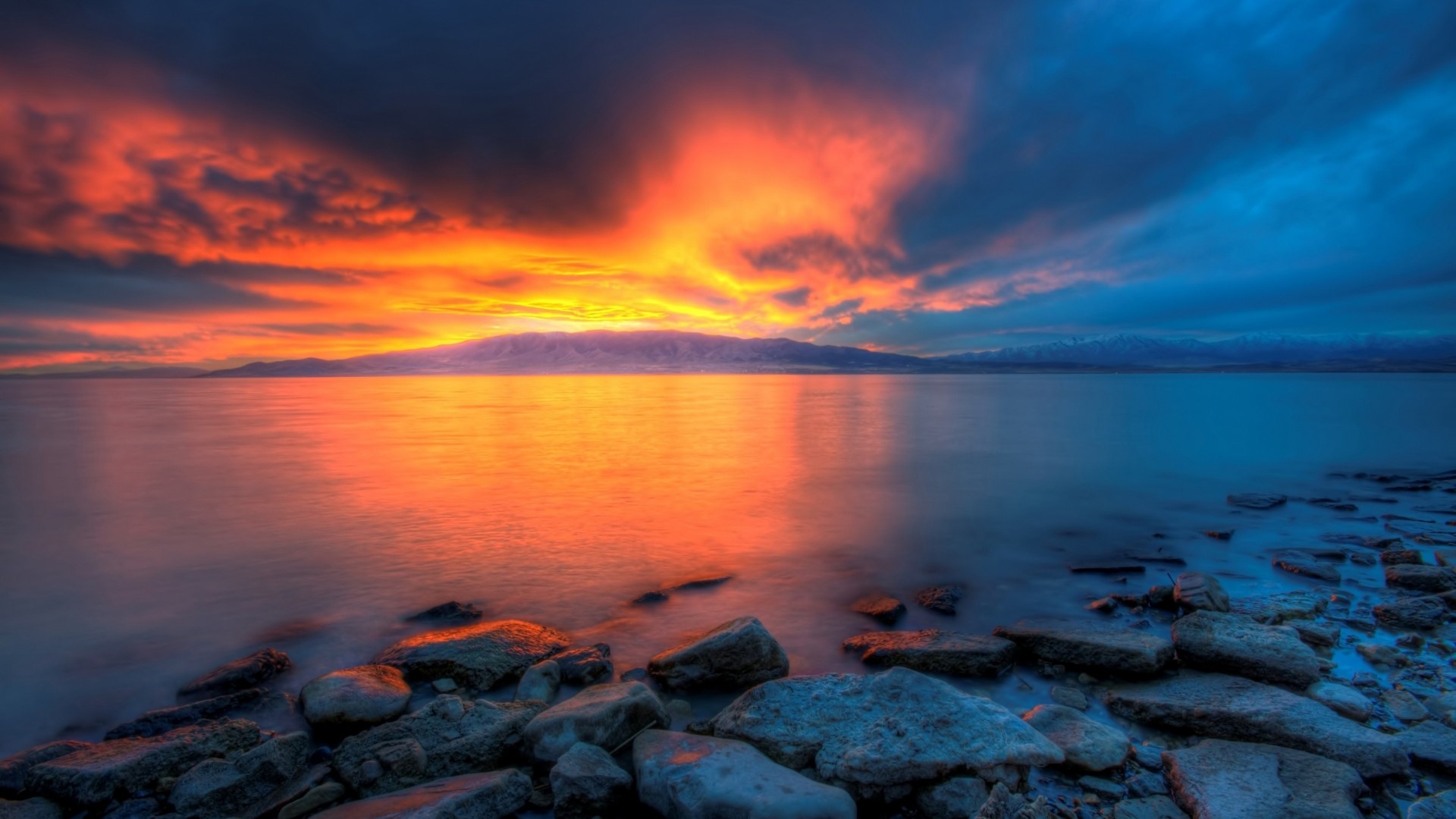 Sunset over a rocky shore and calm water HD Wallpaper