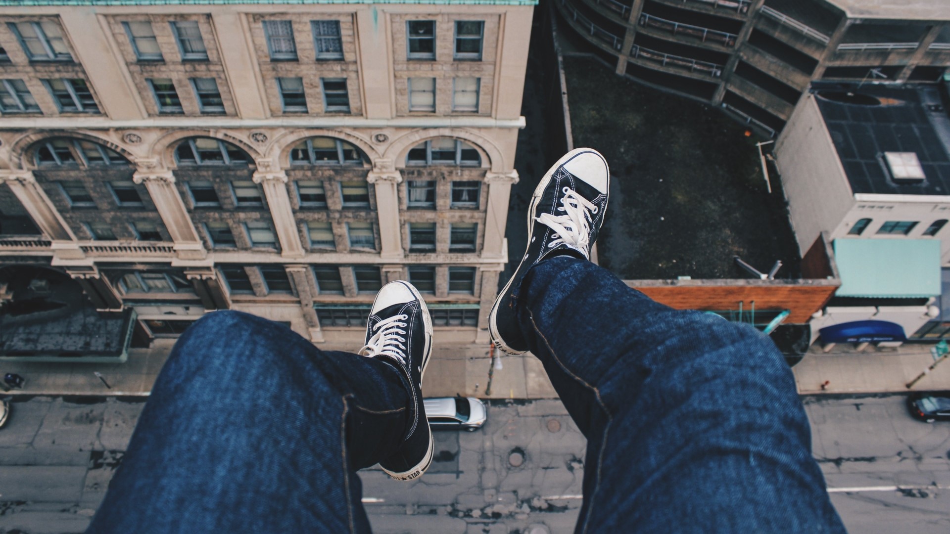 Person sitting on edge of building overlooking city HD Wallpaper