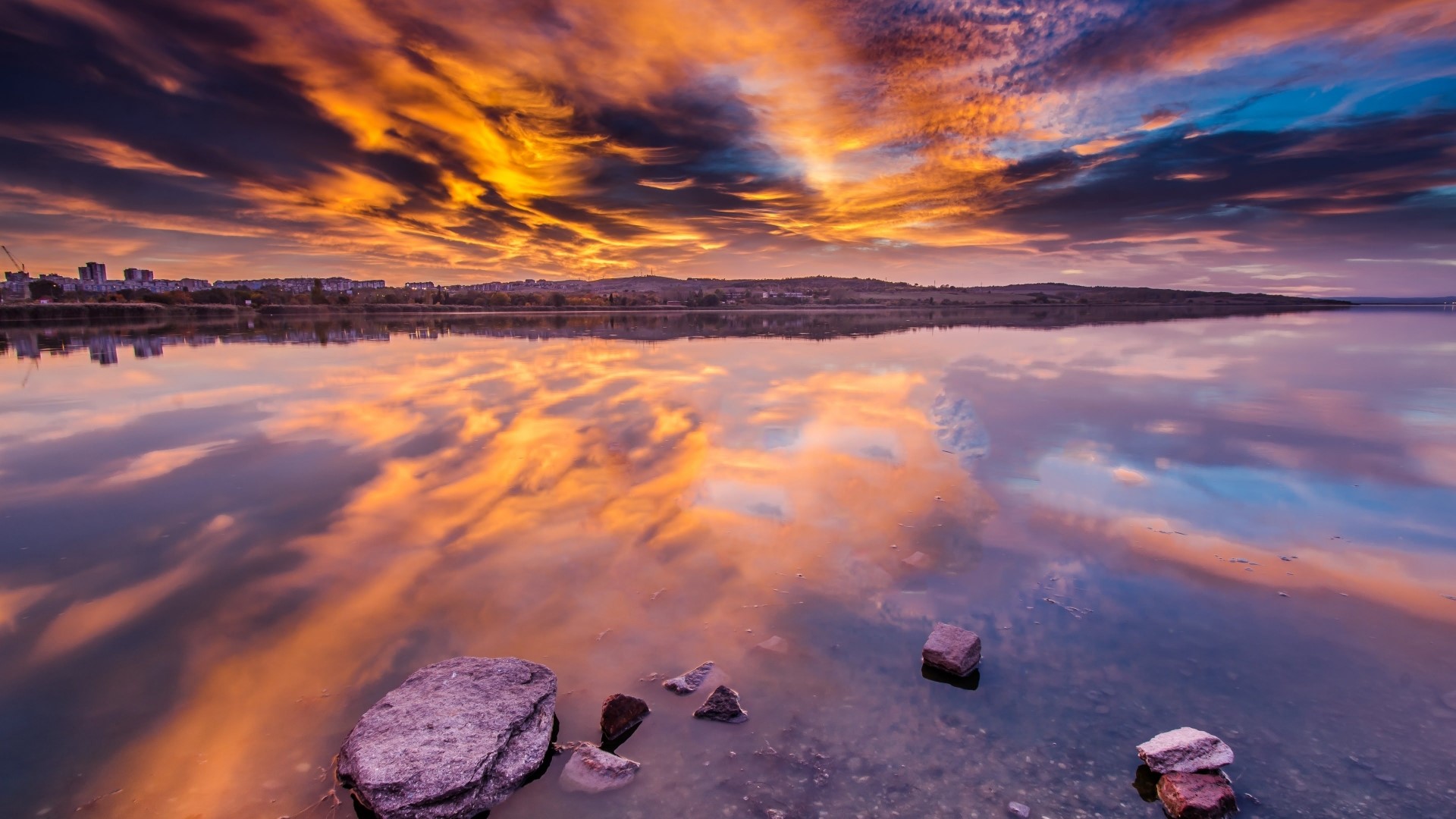 Sunset mirroring over a lake with city skyline HD Wallpaper