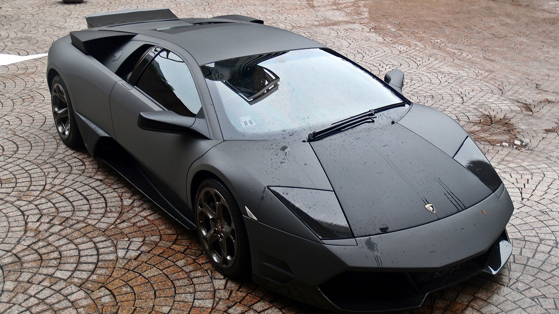 Matte black Lamborghini parked on cobblestone HD Wallpaper