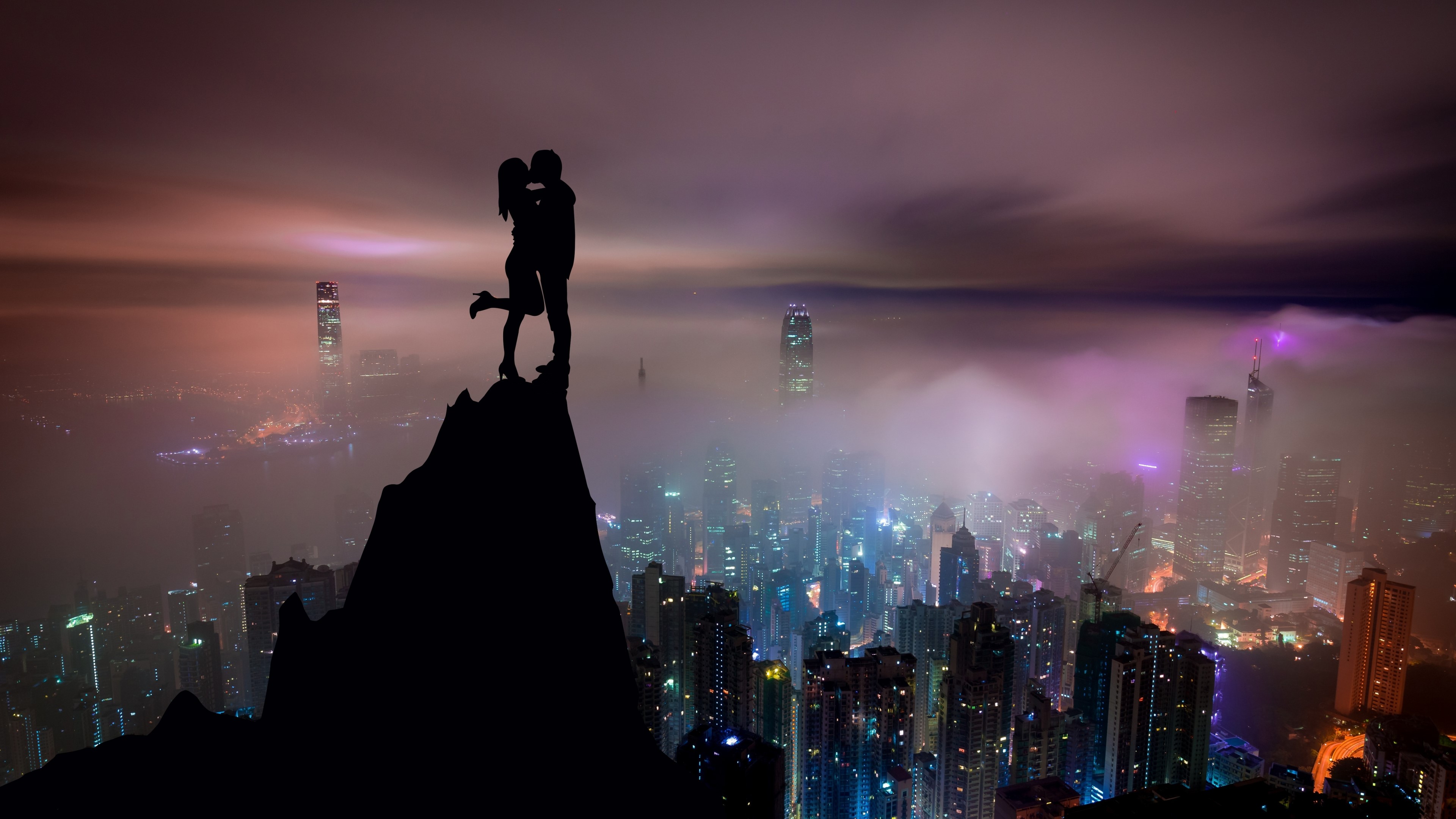 4K Silhouettes of a Couple Kissing on a Mountain Peak Overlooking a City HD Wallpaper
