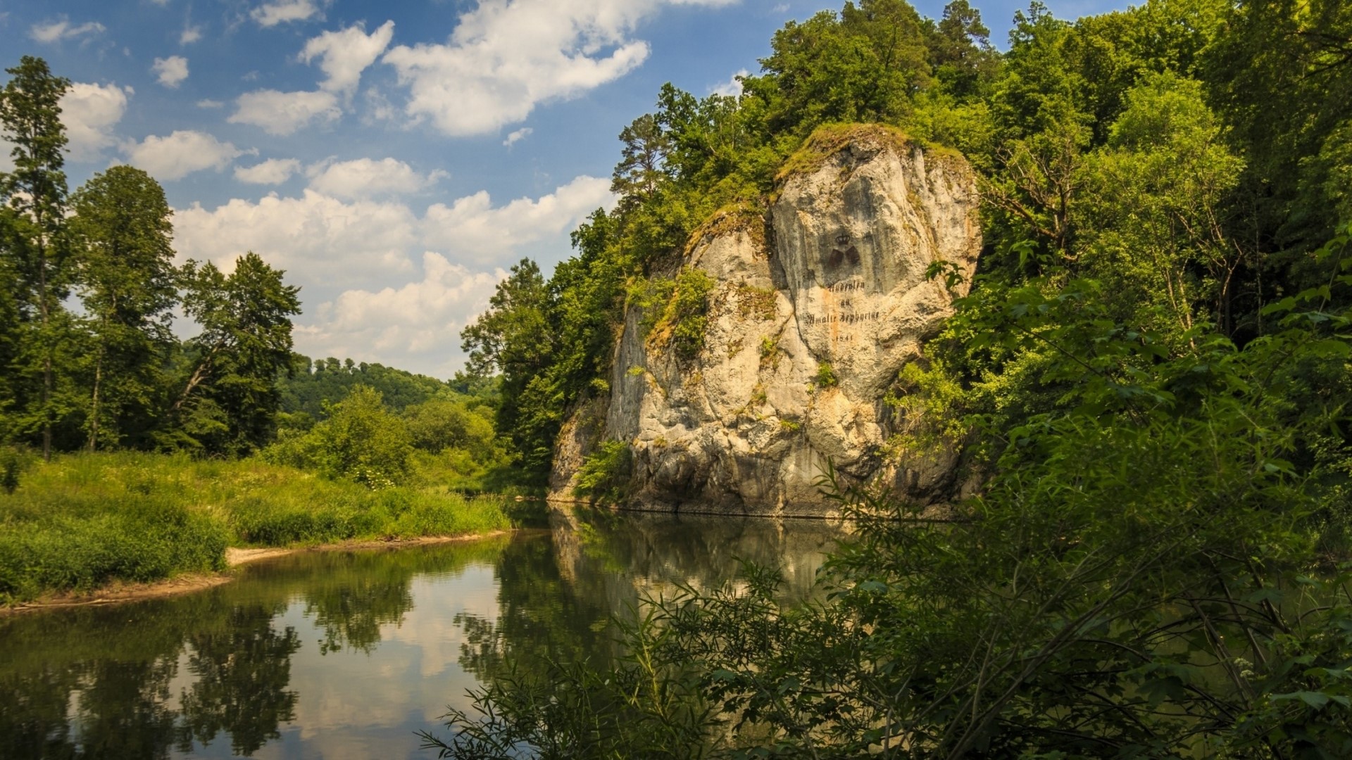 River flowing past a rocky cliff face with trees HD Wallpaper