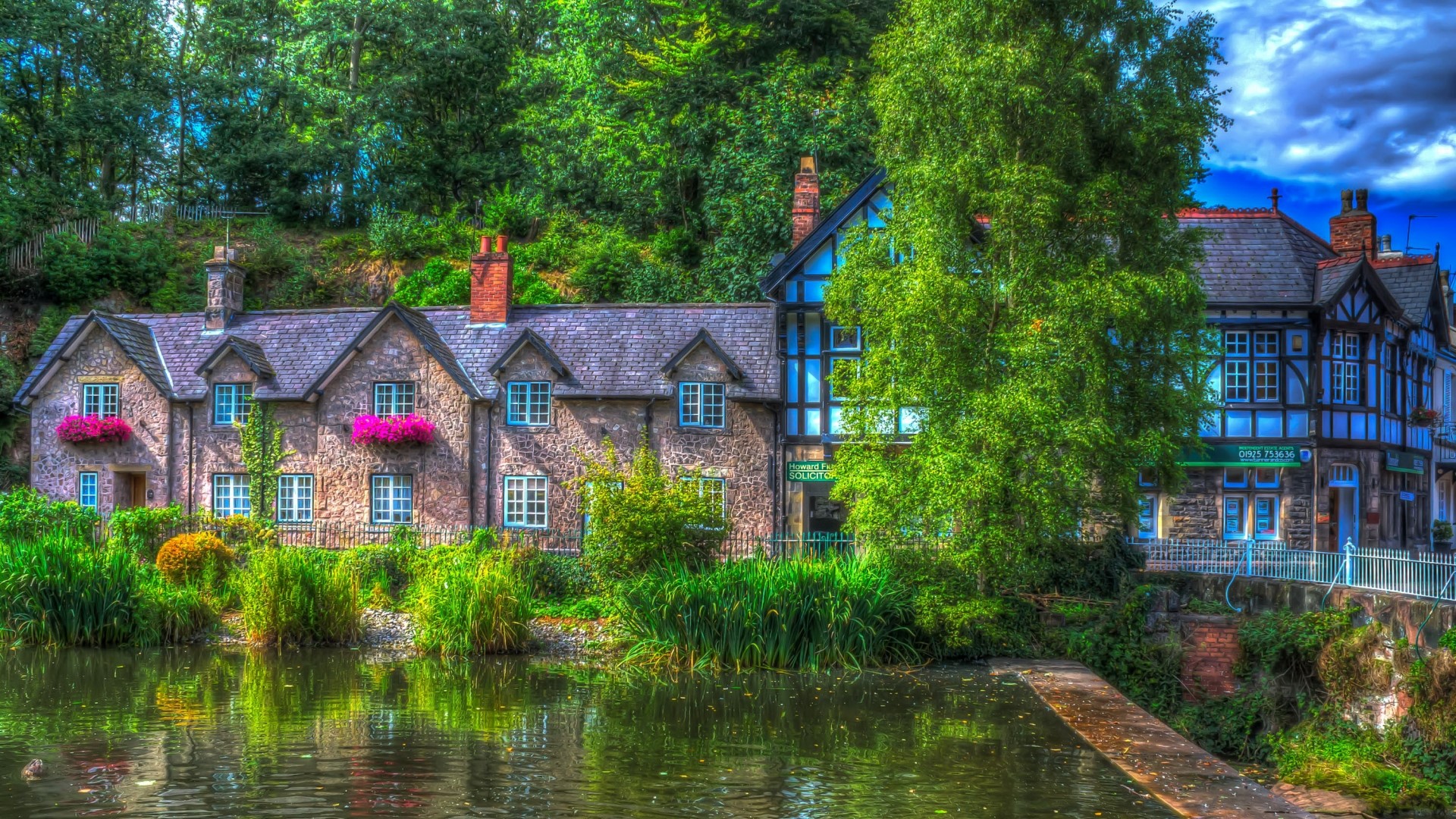 Stone houses by a pond with lush greenery HD Wallpaper