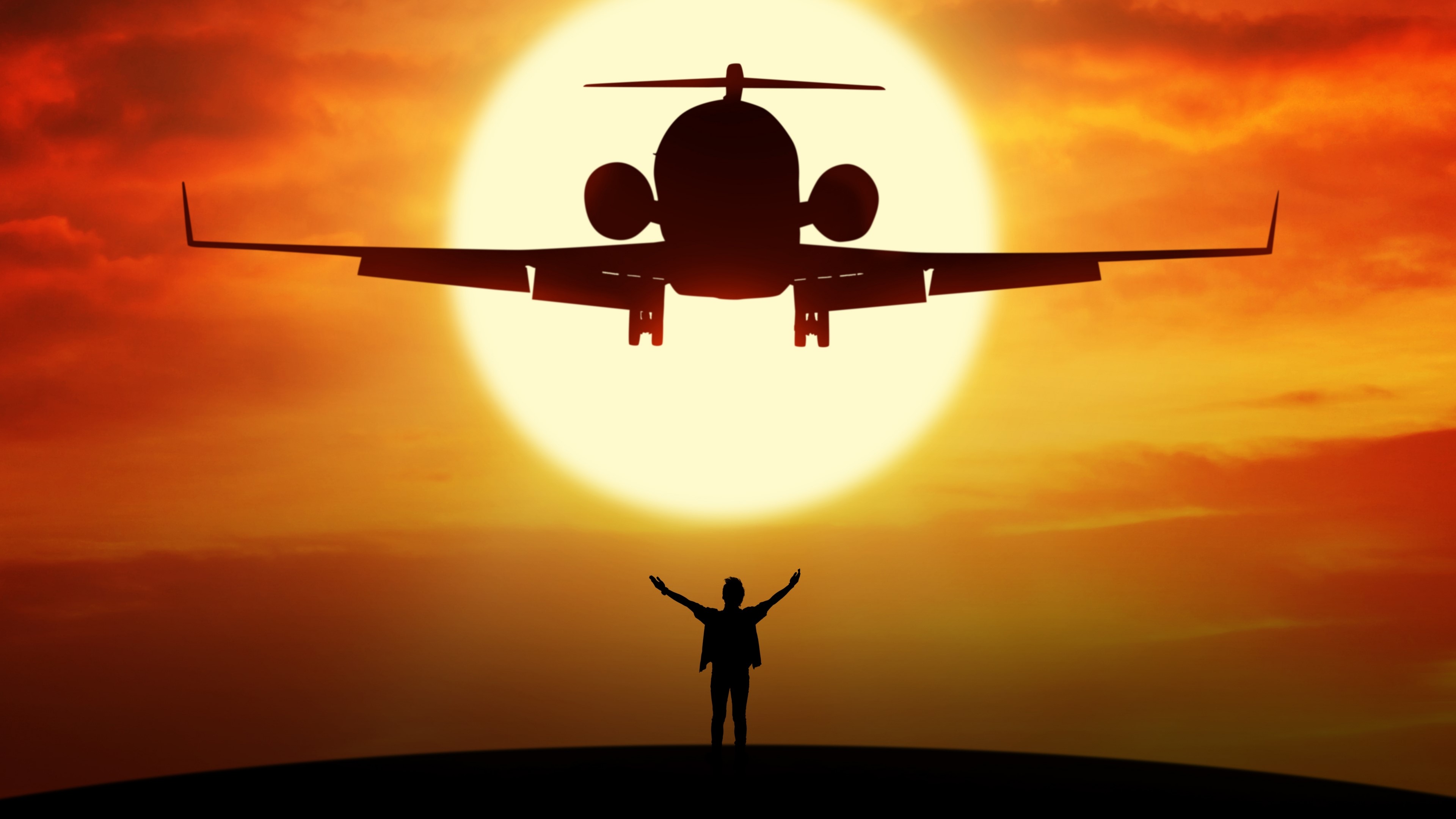 Silhouette of a person with arms raised before a landing airplane at sunset HD Wallpaper