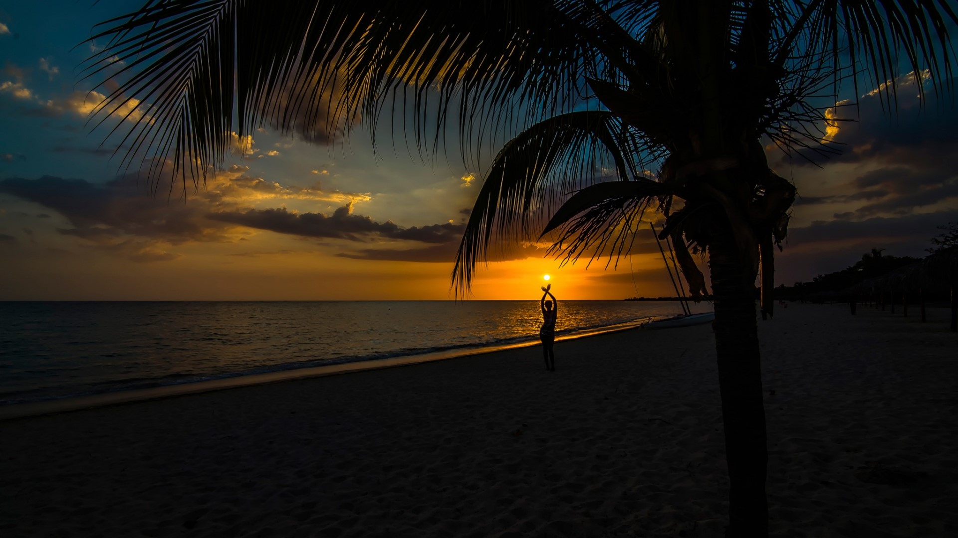 Silhouette of a person holding the sun on a beach at sunset HD Wallpaper