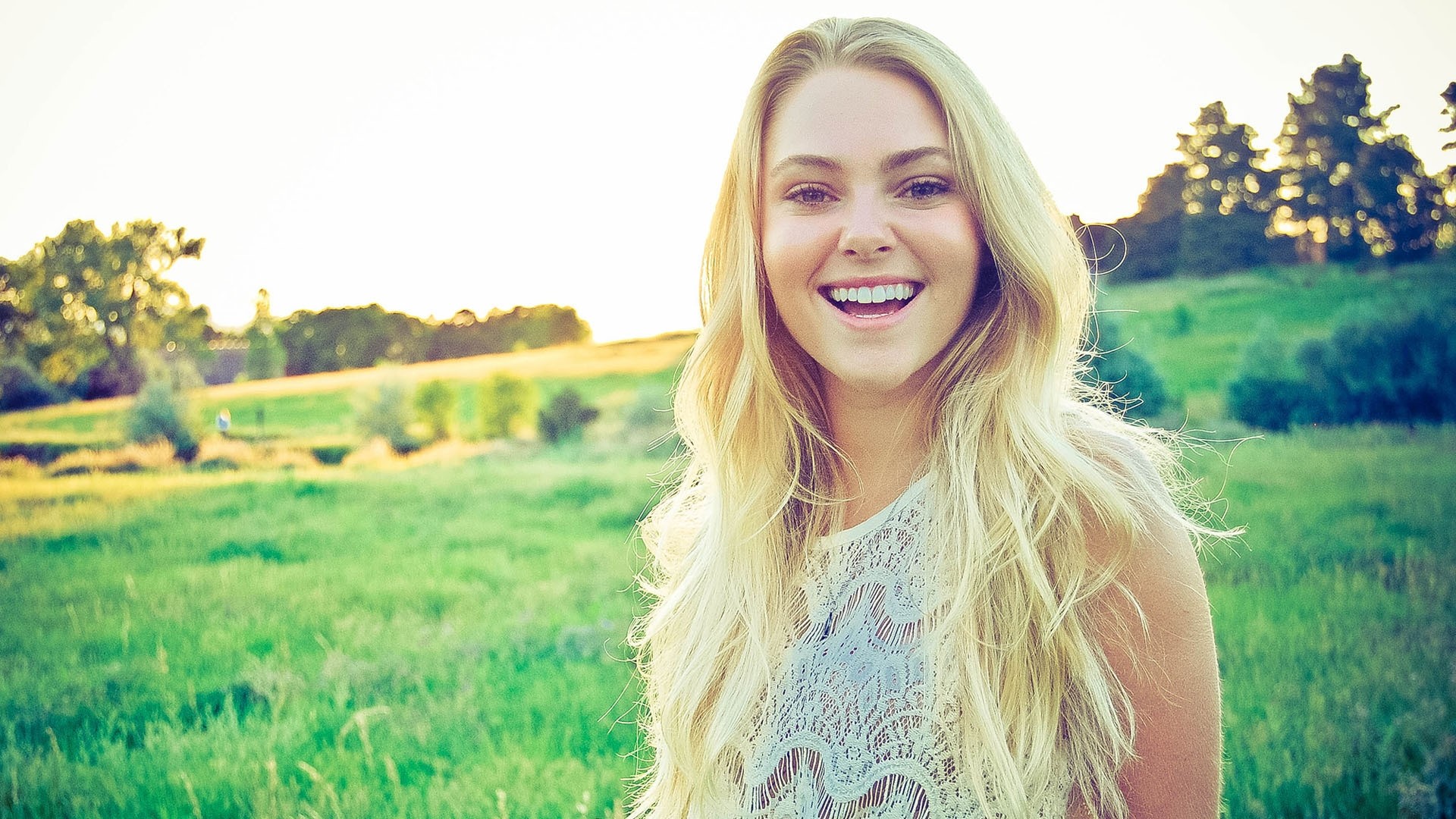 A young woman with blonde hair smiling in a field HD Wallpaper