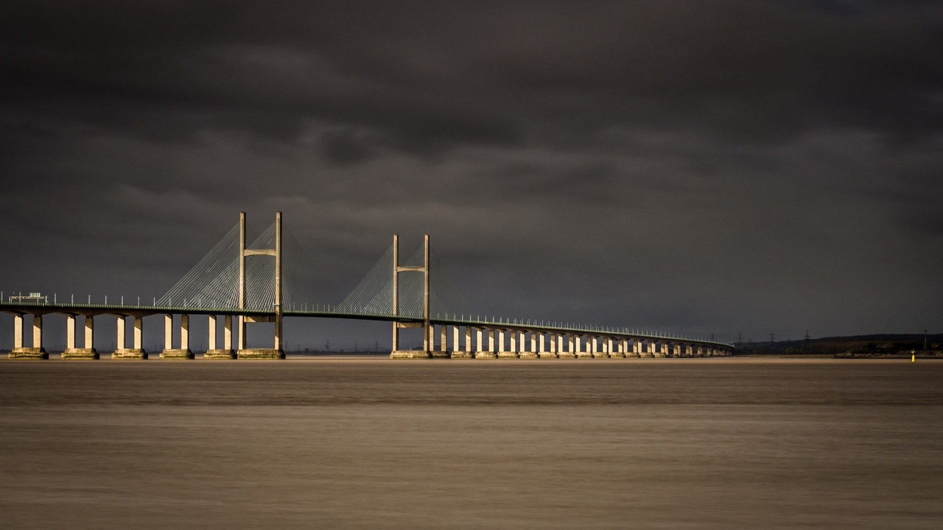 Cable-stayed bridge over water under dark clouds HD Wallpaper