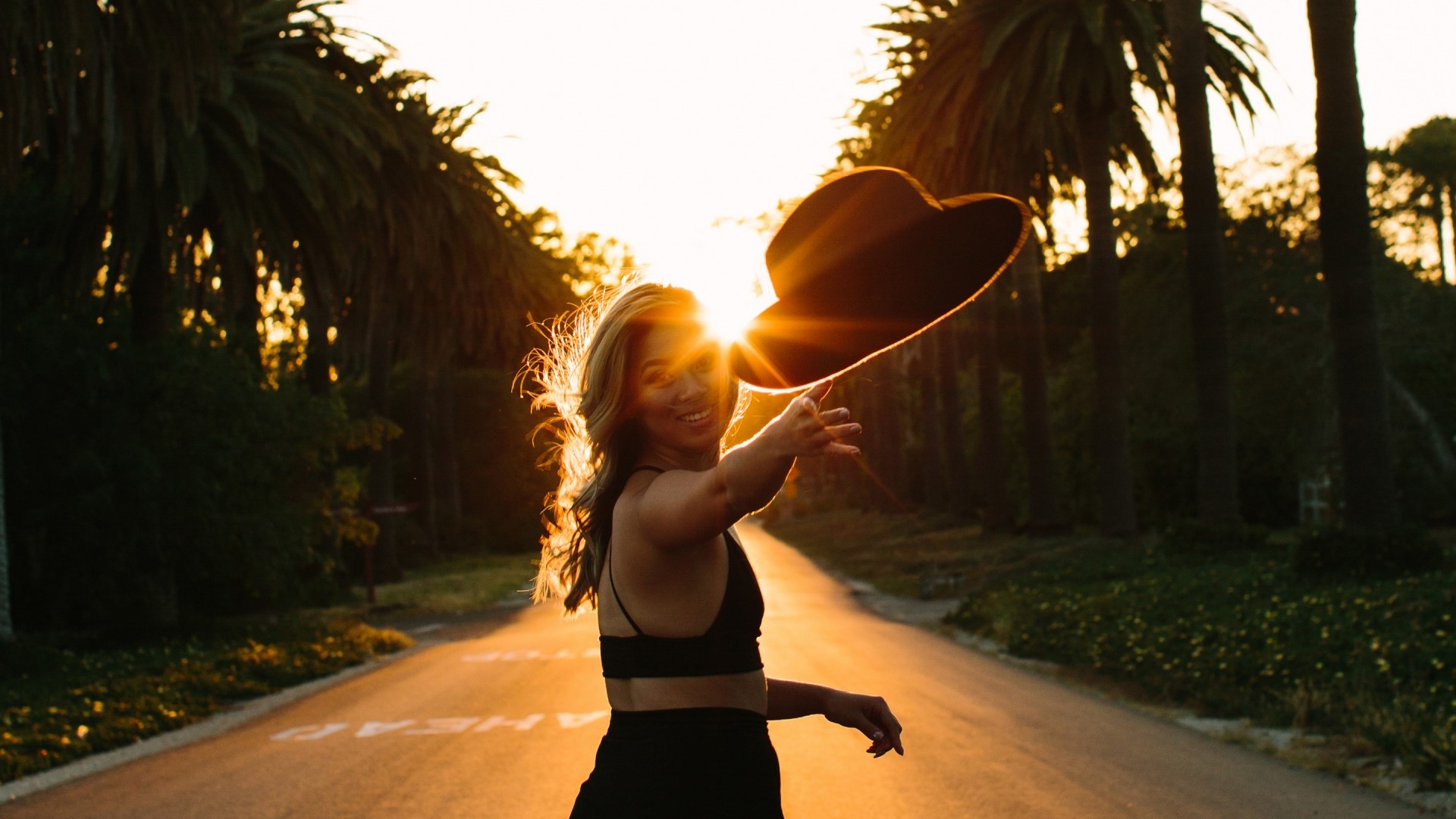 Woman in black outfit throwing hat at sunset HD Wallpaper