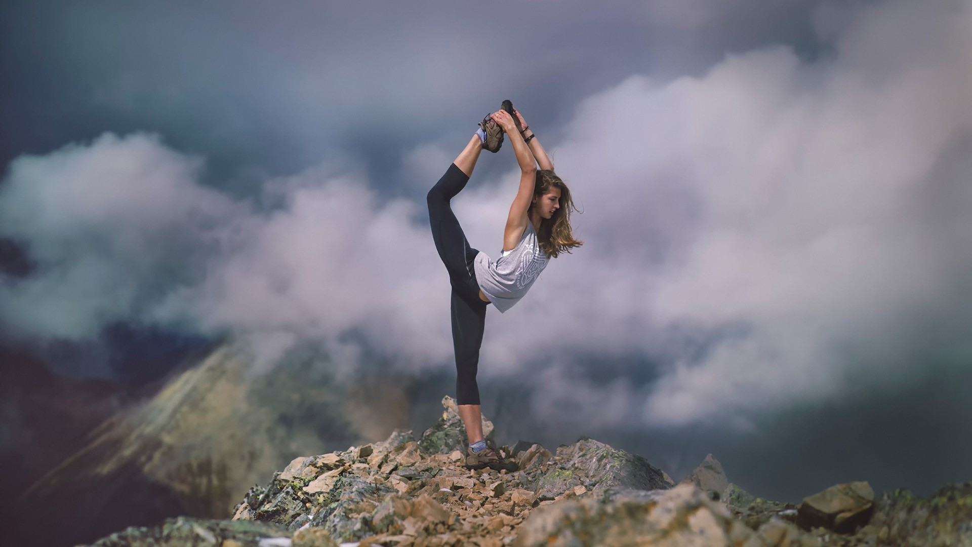 Woman performing yoga on a rocky mountain peak HD Wallpaper