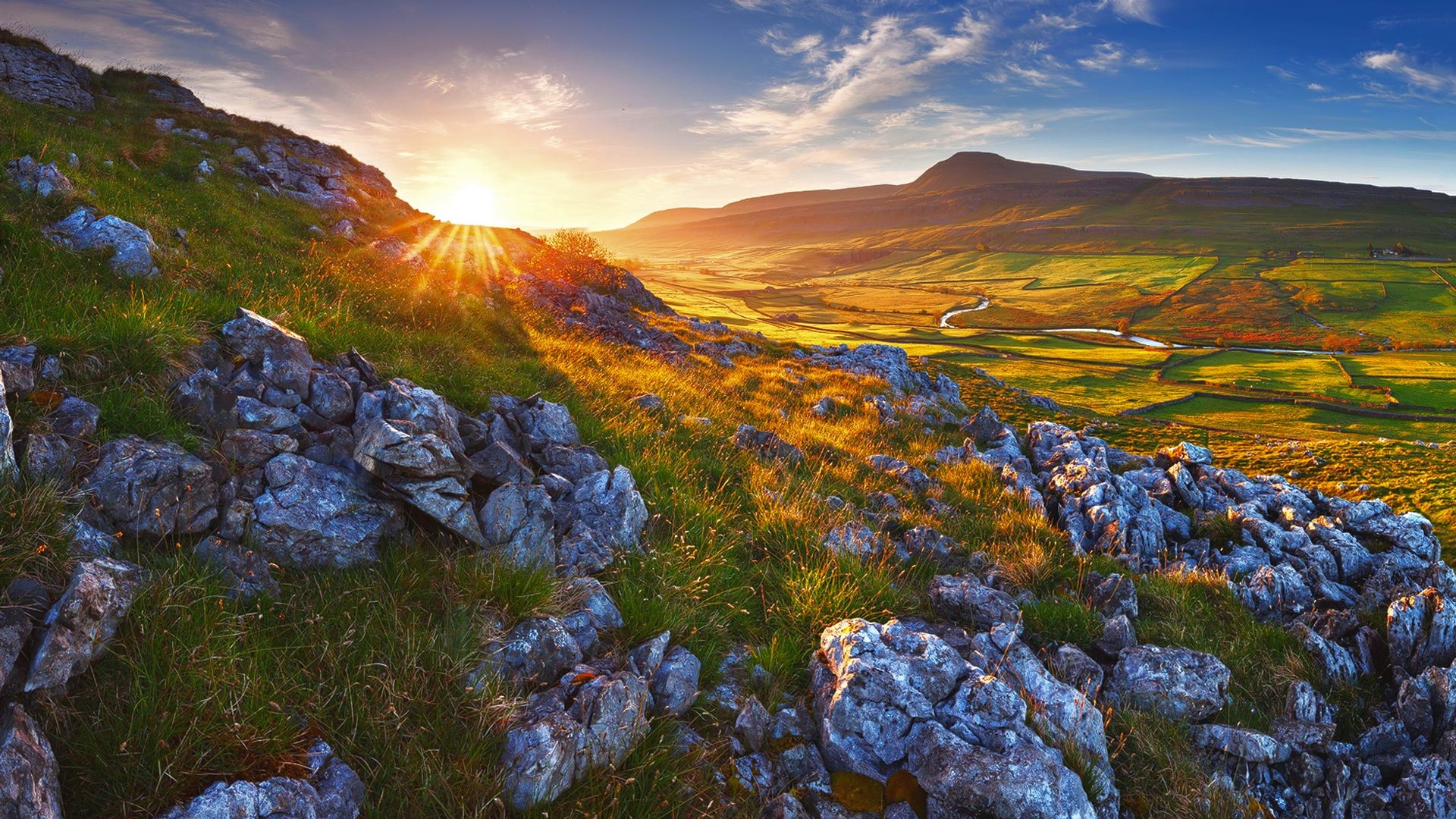 Sunrise over a rocky, grassy hill overlooking a valley HD Wallpaper