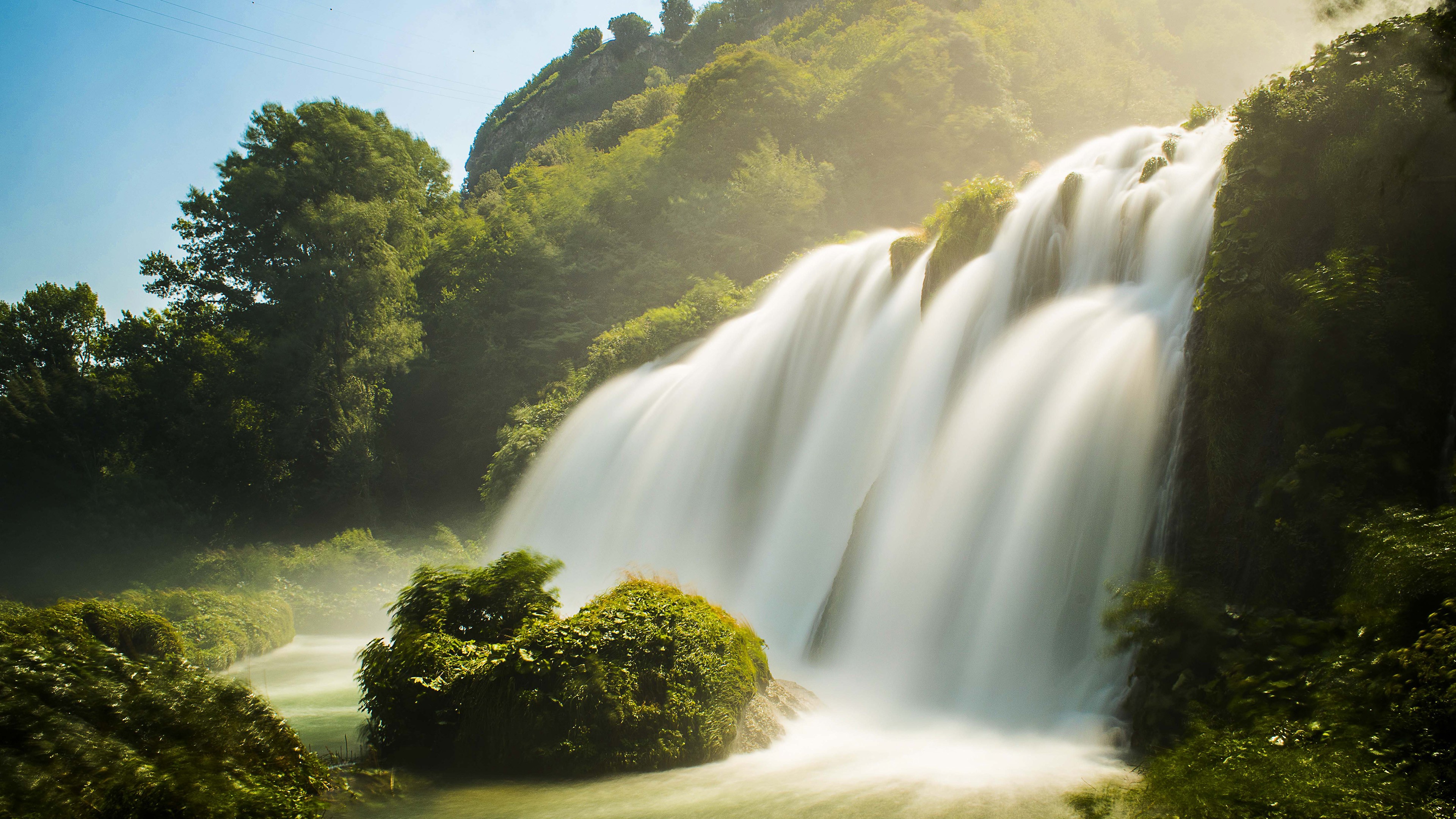 Waterfall in a forest with sunlight HD Wallpaper