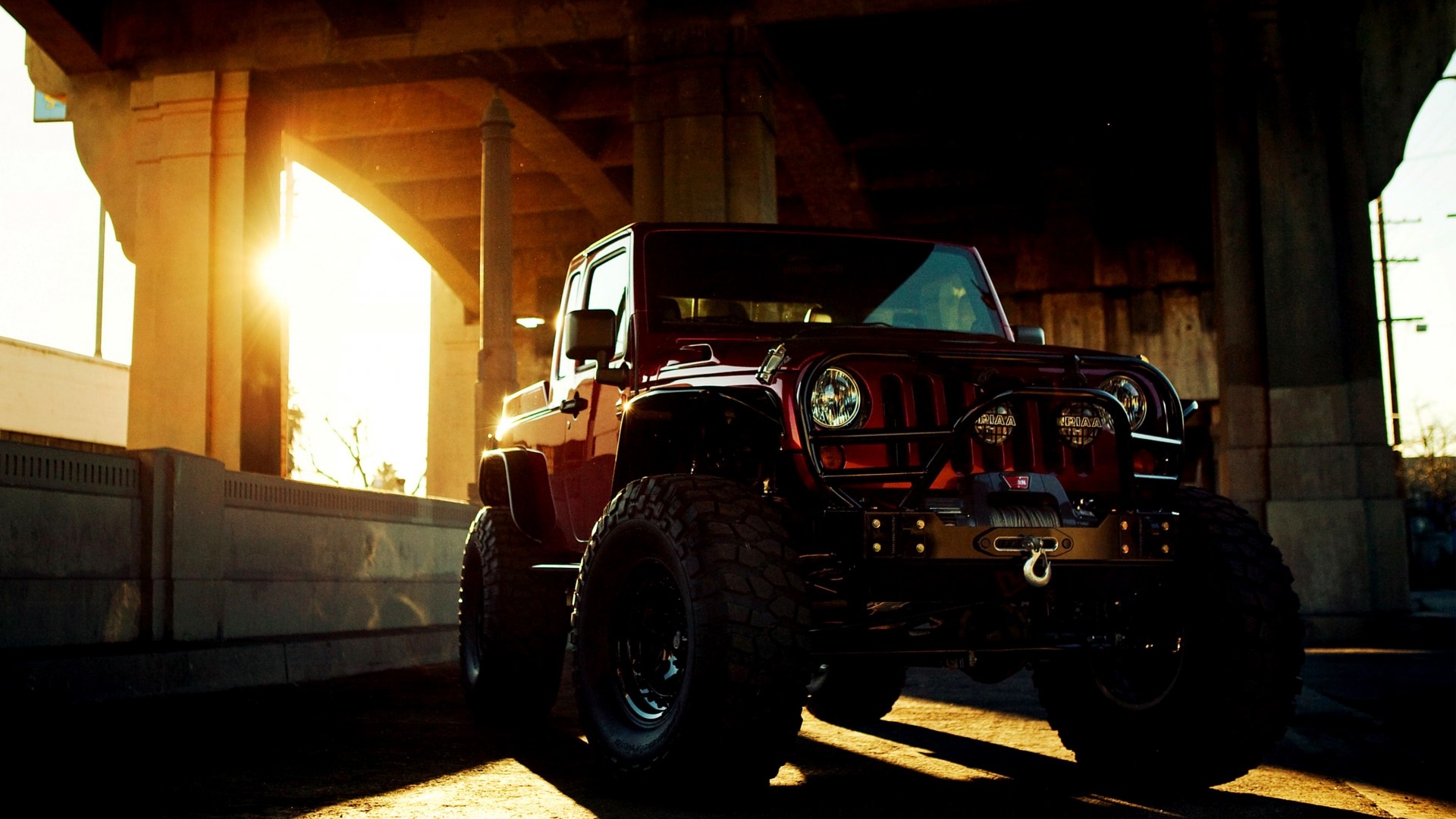 Red Jeep Wrangler with large tires under a bridge HD Wallpaper