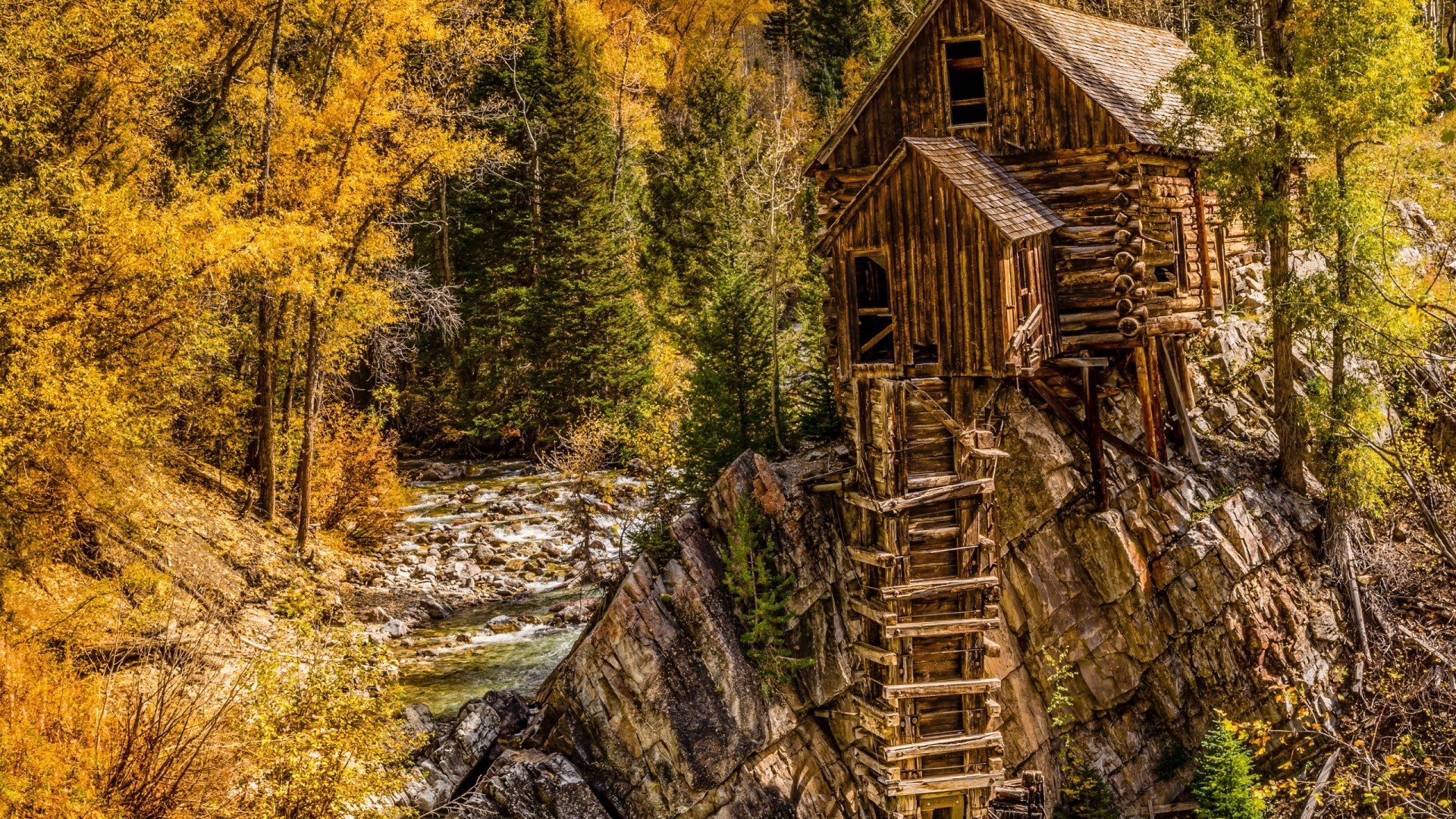 Old wooden house on a cliff by a river in autumn HD Wallpaper