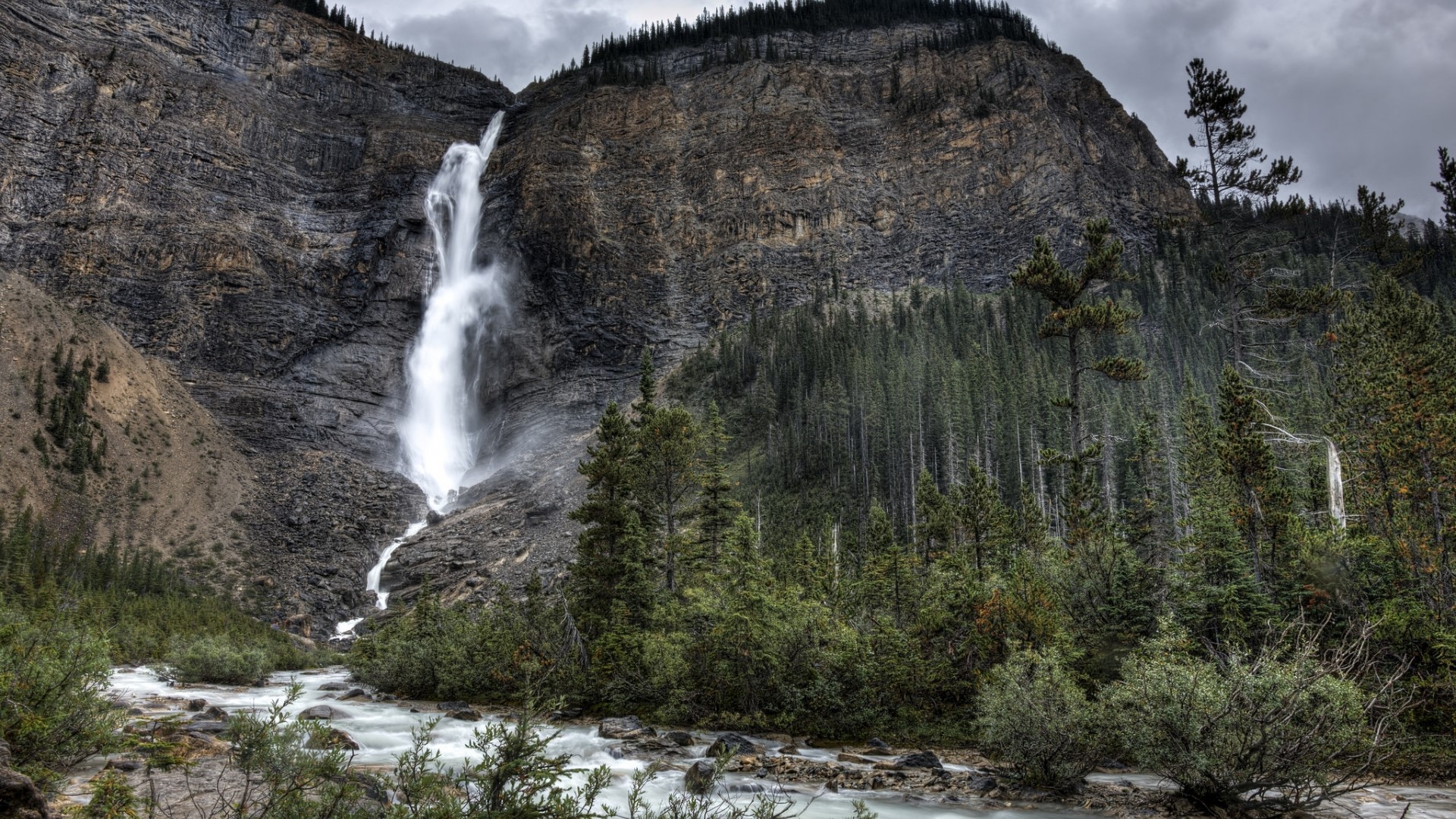 Waterfall cascading down a rocky mountain with a river HD Wallpaper