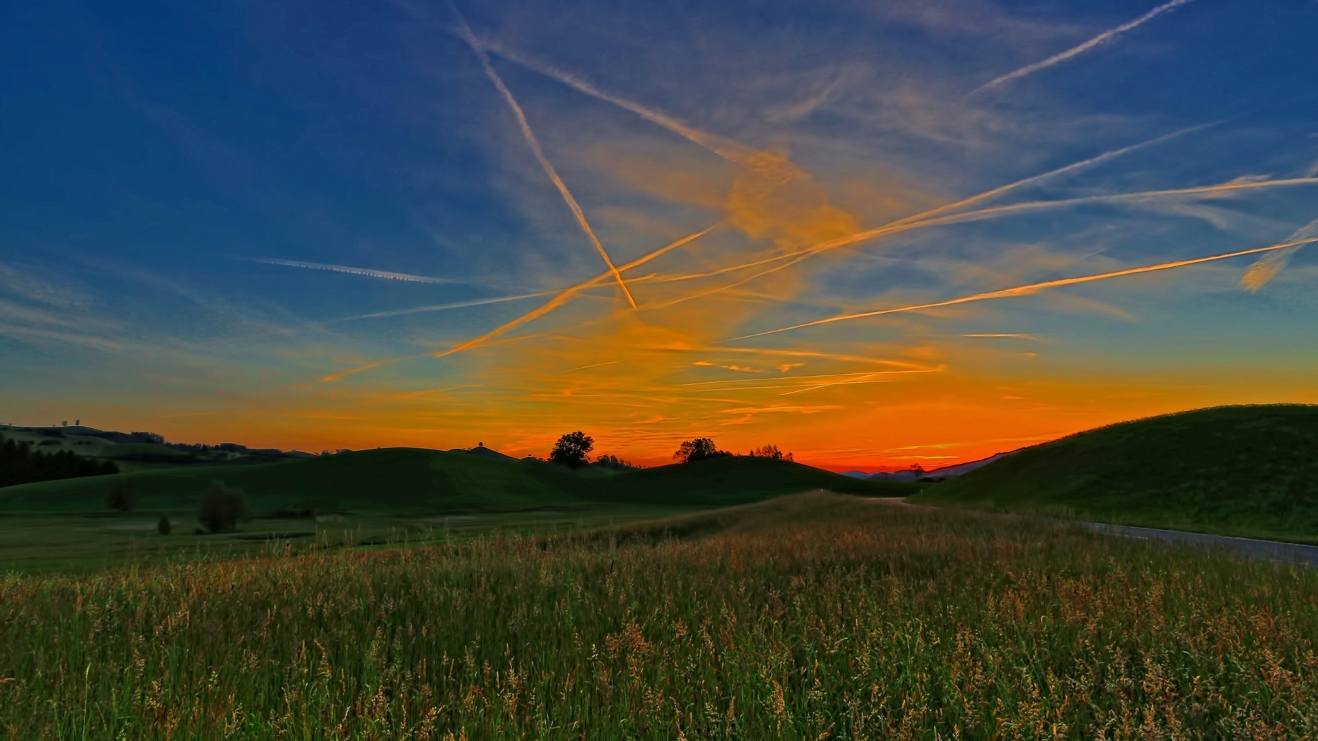 Sunset over rolling green hills with contrails HD Wallpaper