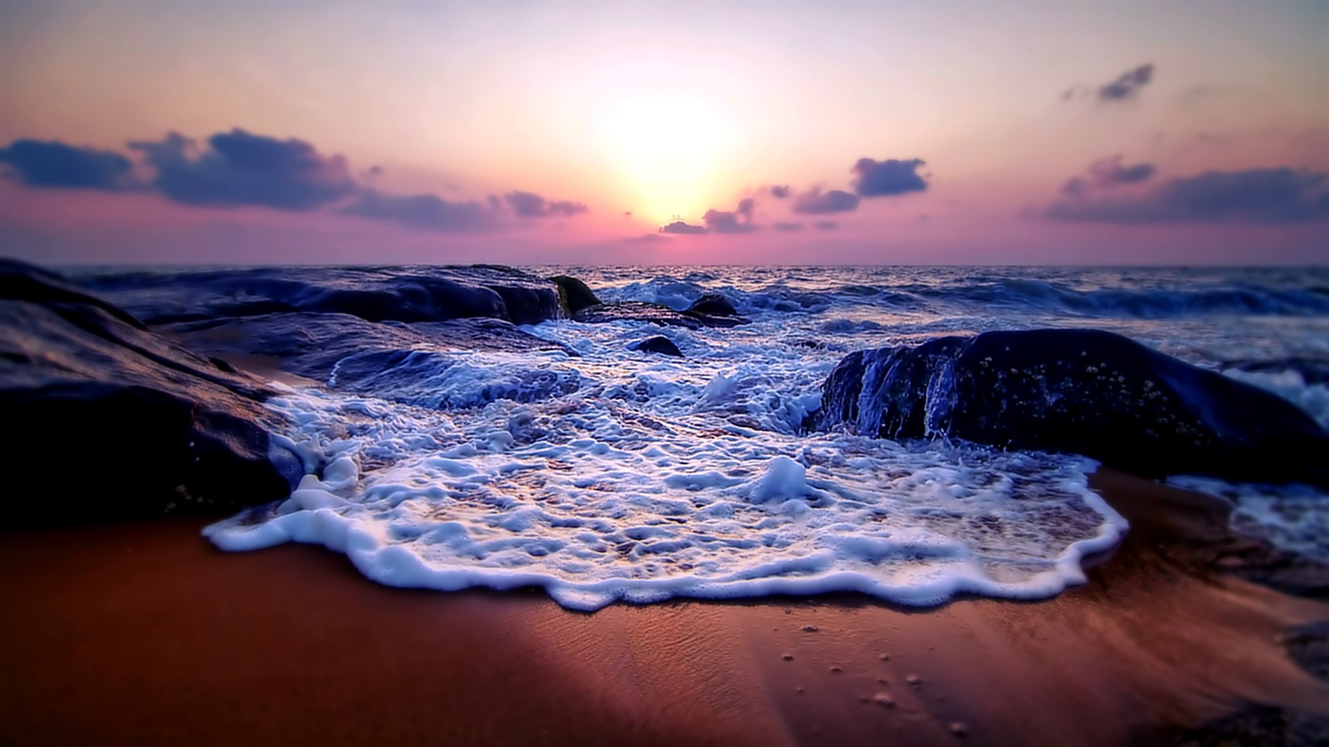 Sunset over the ocean with waves crashing on rocks HD Wallpaper