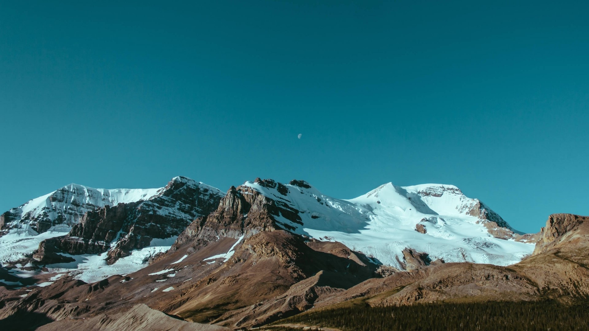 Snow-capped mountains under a clear blue sky with a crescent moon HD Wallpaper
