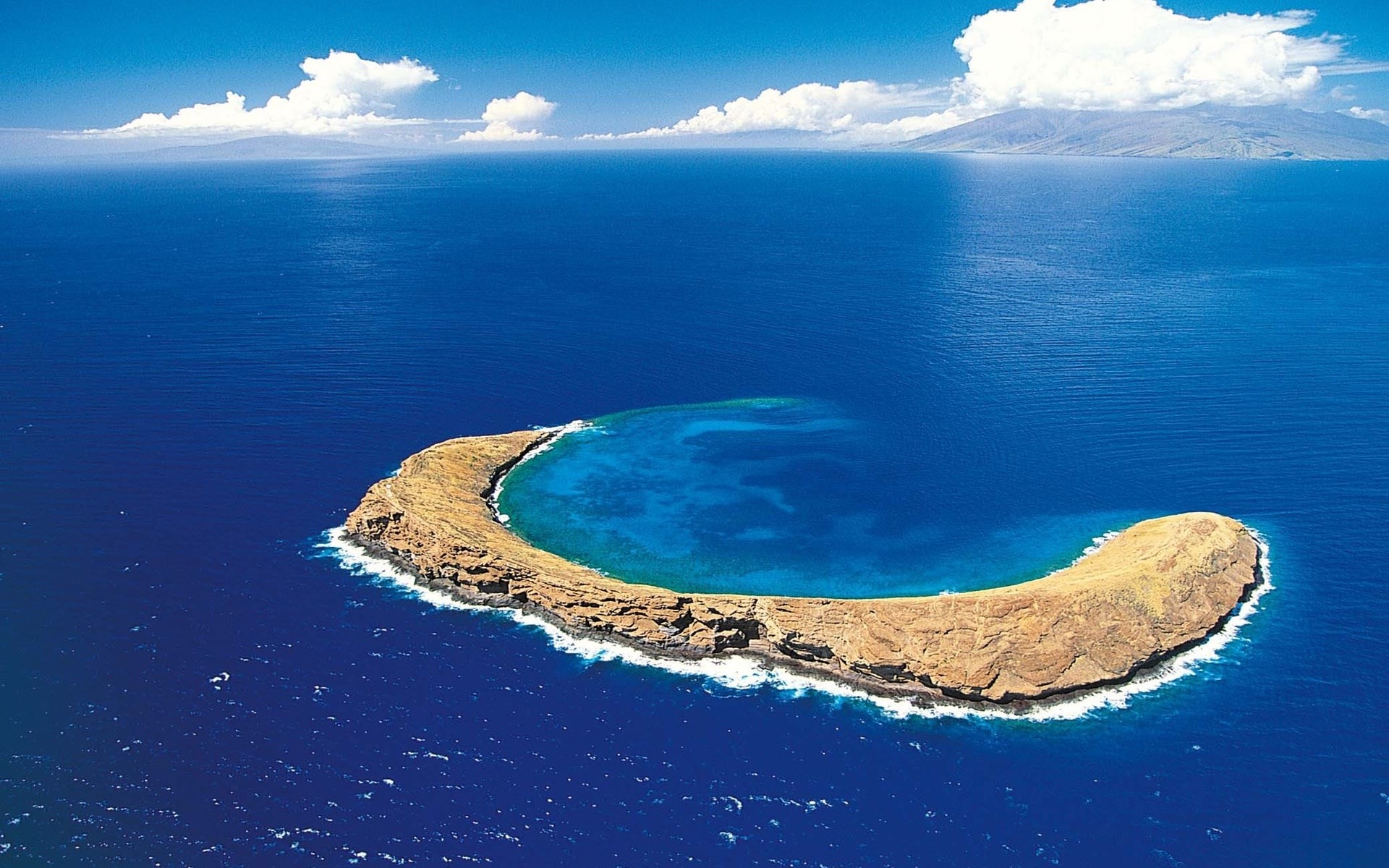 Aerial view of a crescent-shaped island in the ocean HD Wallpaper