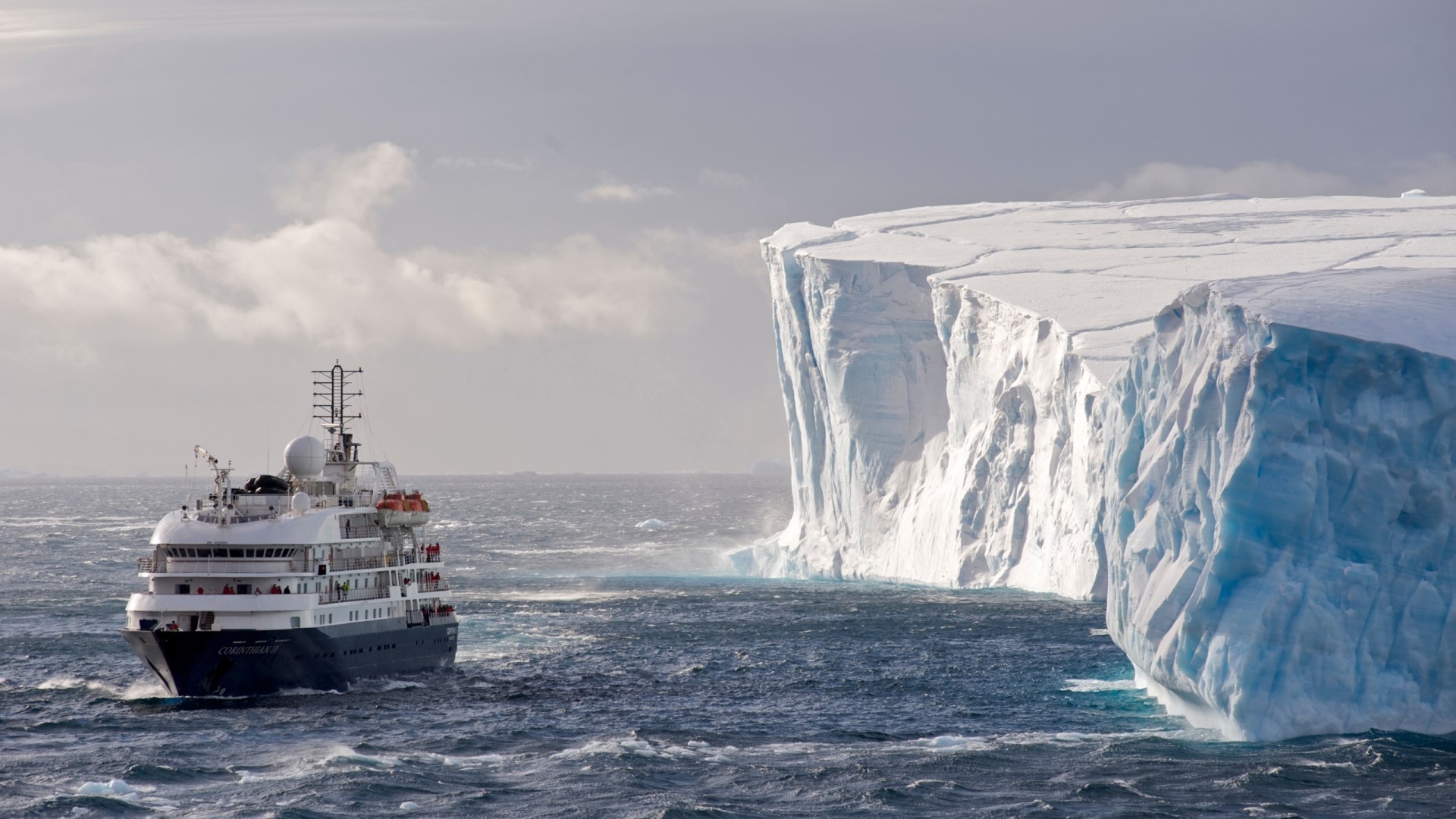 Ship sailing near a large iceberg in Antarctica HD Wallpaper