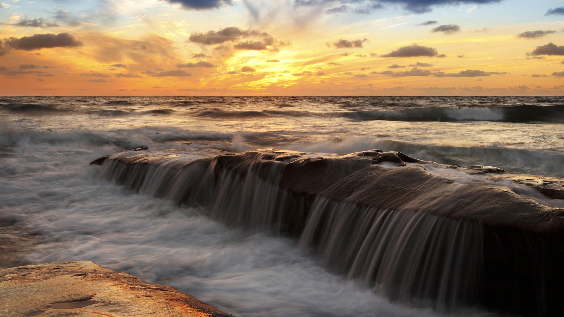 Ocean waves crashing over rocks at sunset HD Wallpaper