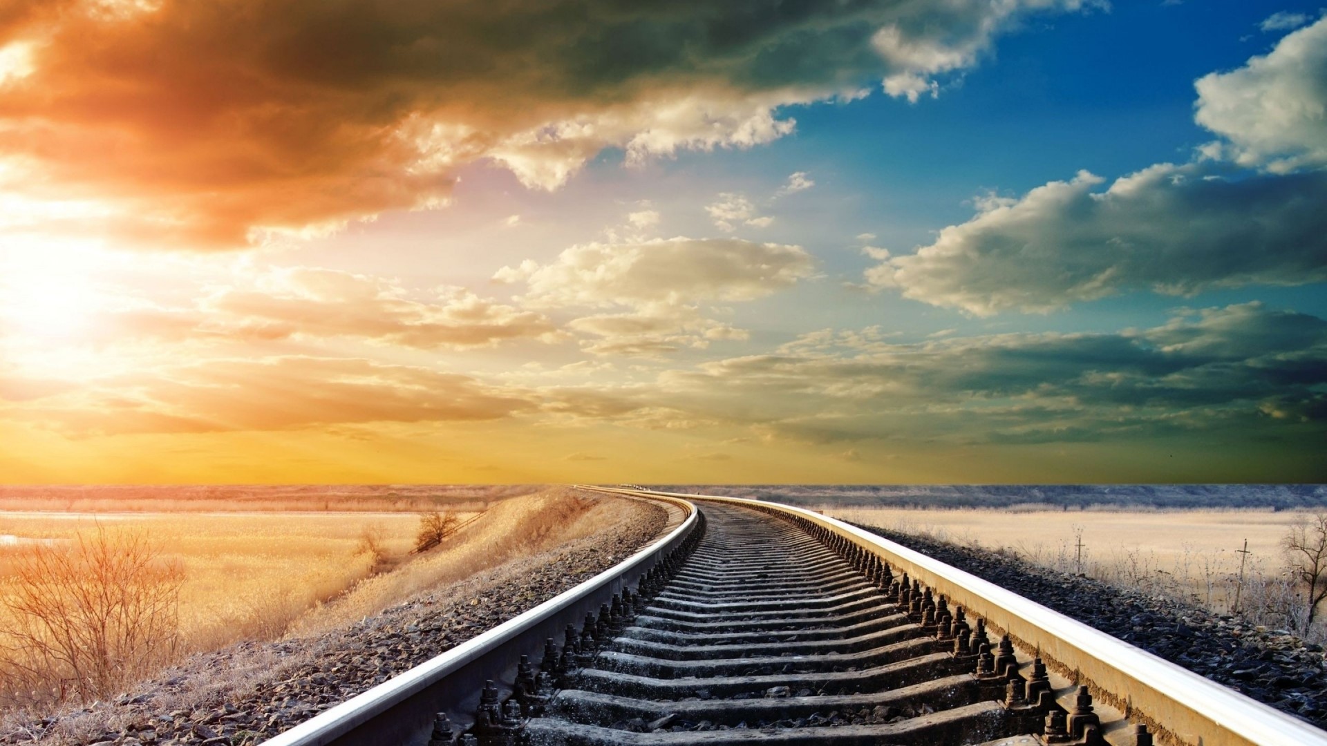 Railroad tracks curving through a landscape at sunset HD Wallpaper