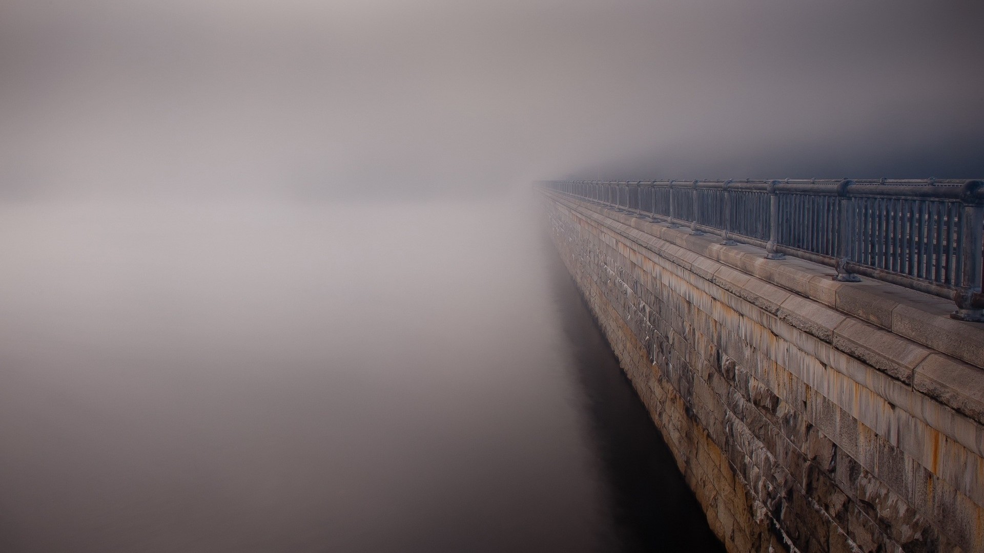 Stone dam wall disappearing into fog HD Wallpaper