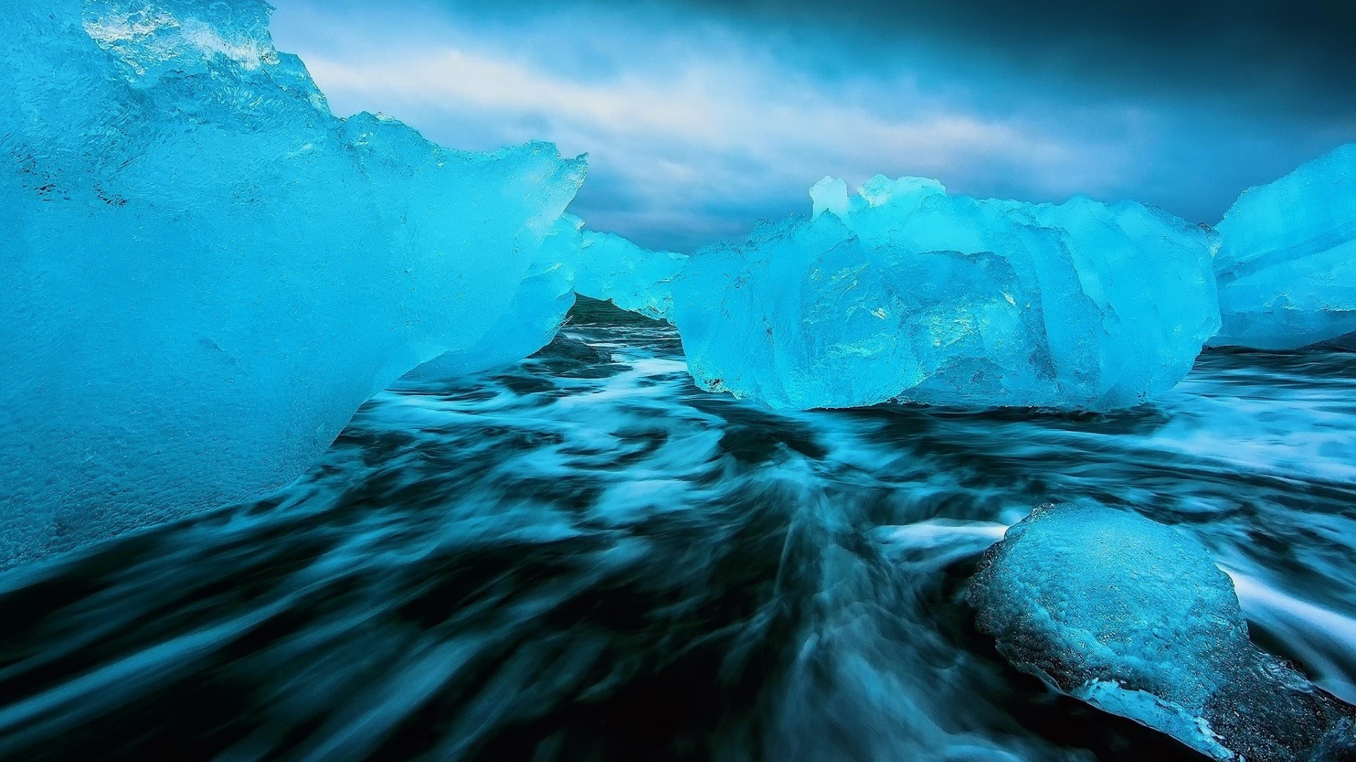 Blue icebergs on a dark beach with waves HD Wallpaper