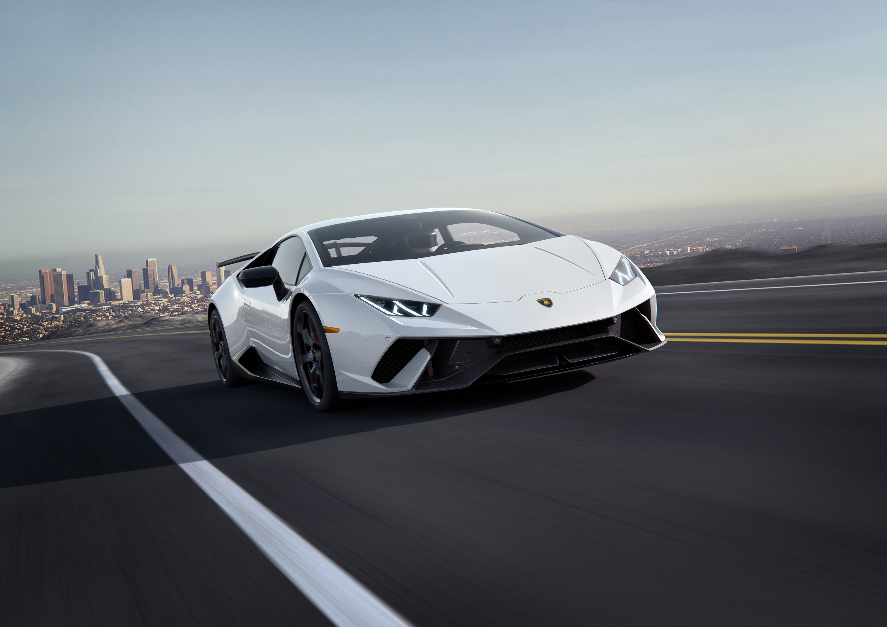 White Lamborghini Huracan driving on a road with city skyline HD Wallpaper